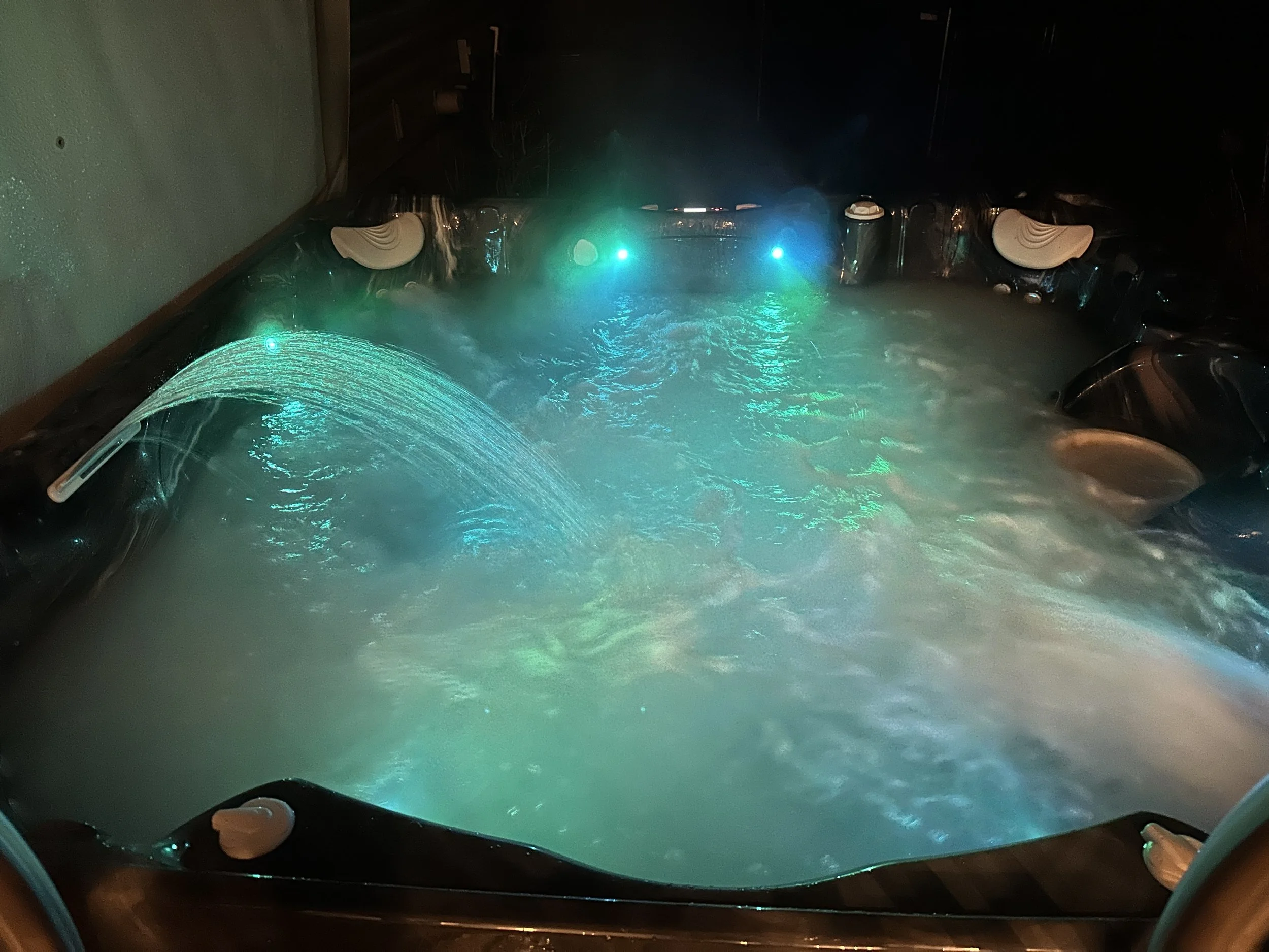  7-person hot tub illuminated by multicolored party lights, creating a vibrant and relaxing ambiance for a perfect evening soak amidst the serene forest setting.