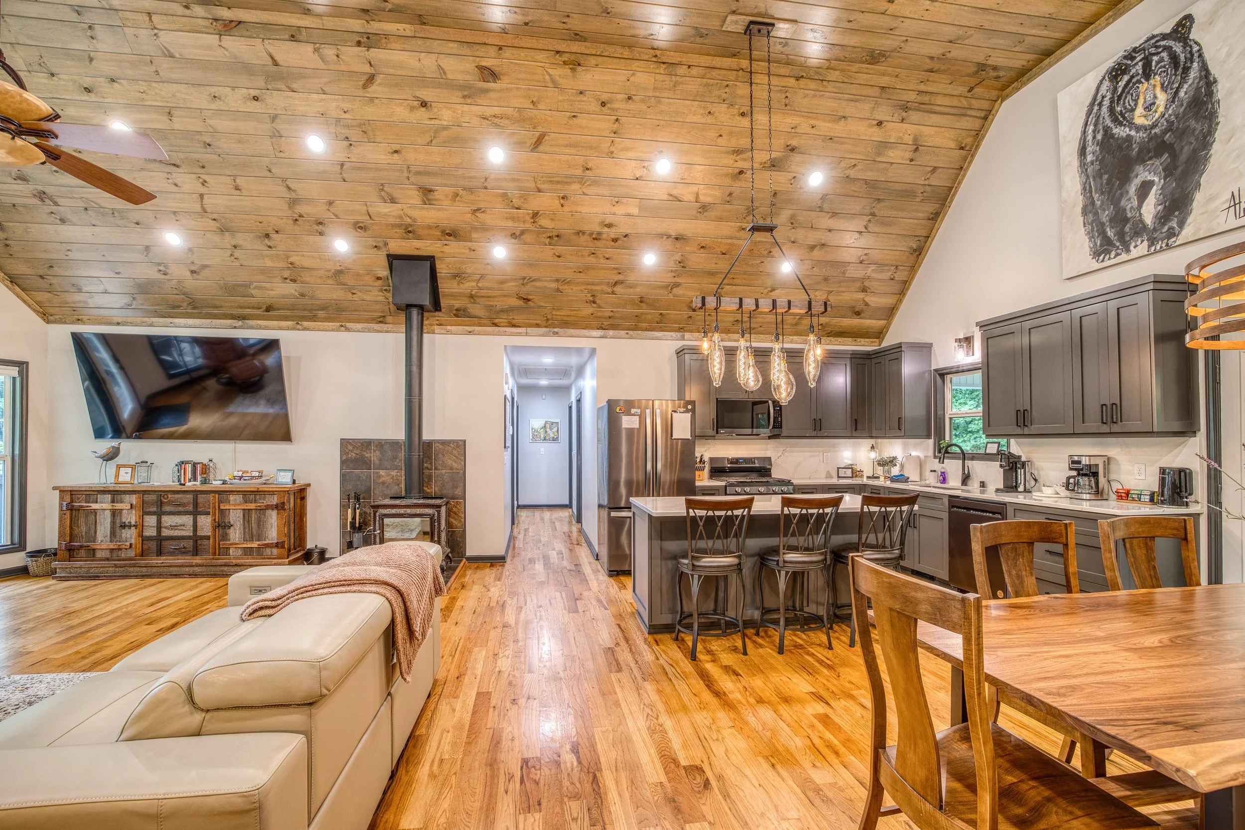 Open concept living space with vaulted ceilings, kitchen island, dining area, and cozy wood-burning stove.
