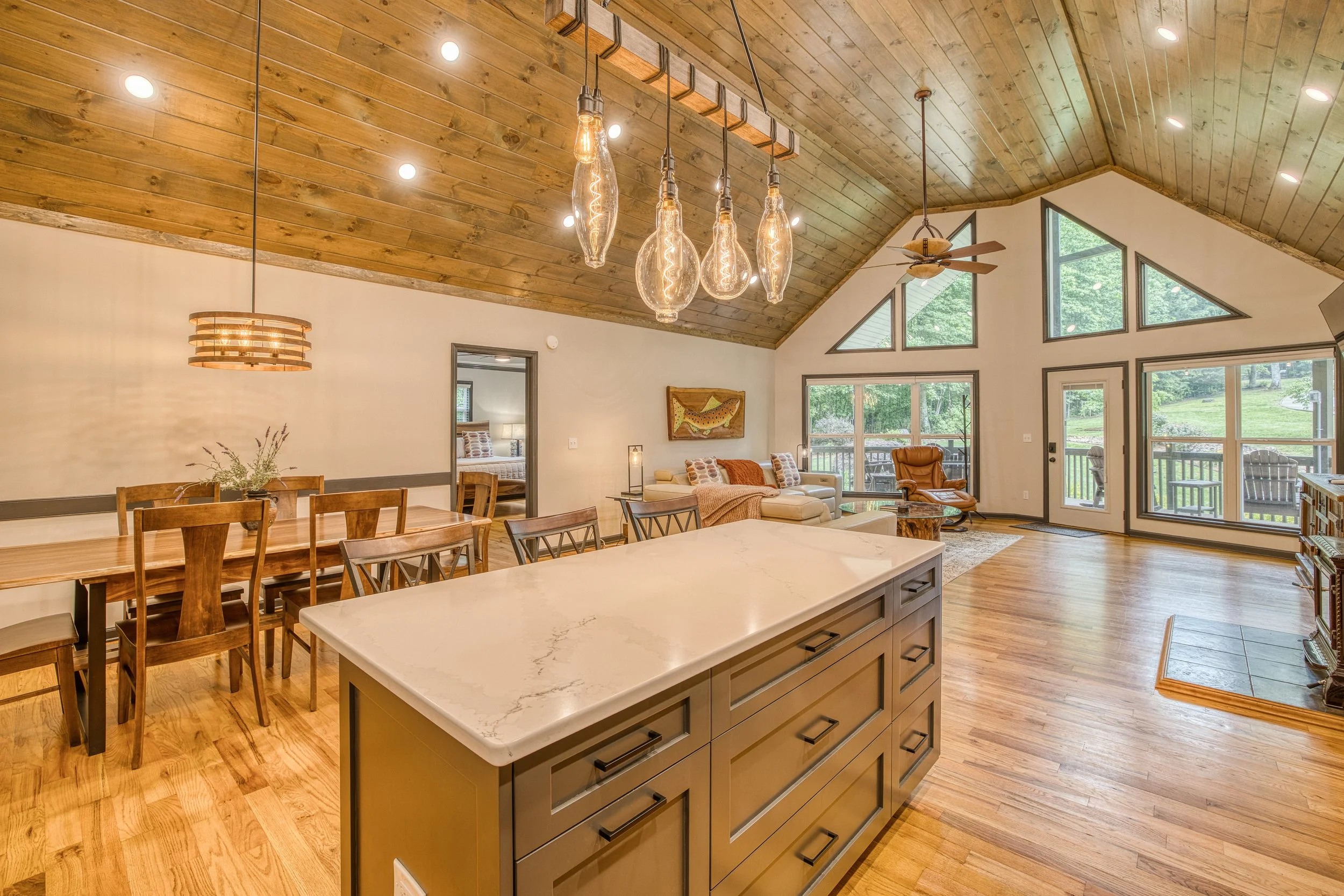 View from kitchen under soaring wooden vaulted ceilings overlooking center island facing dining and living areas