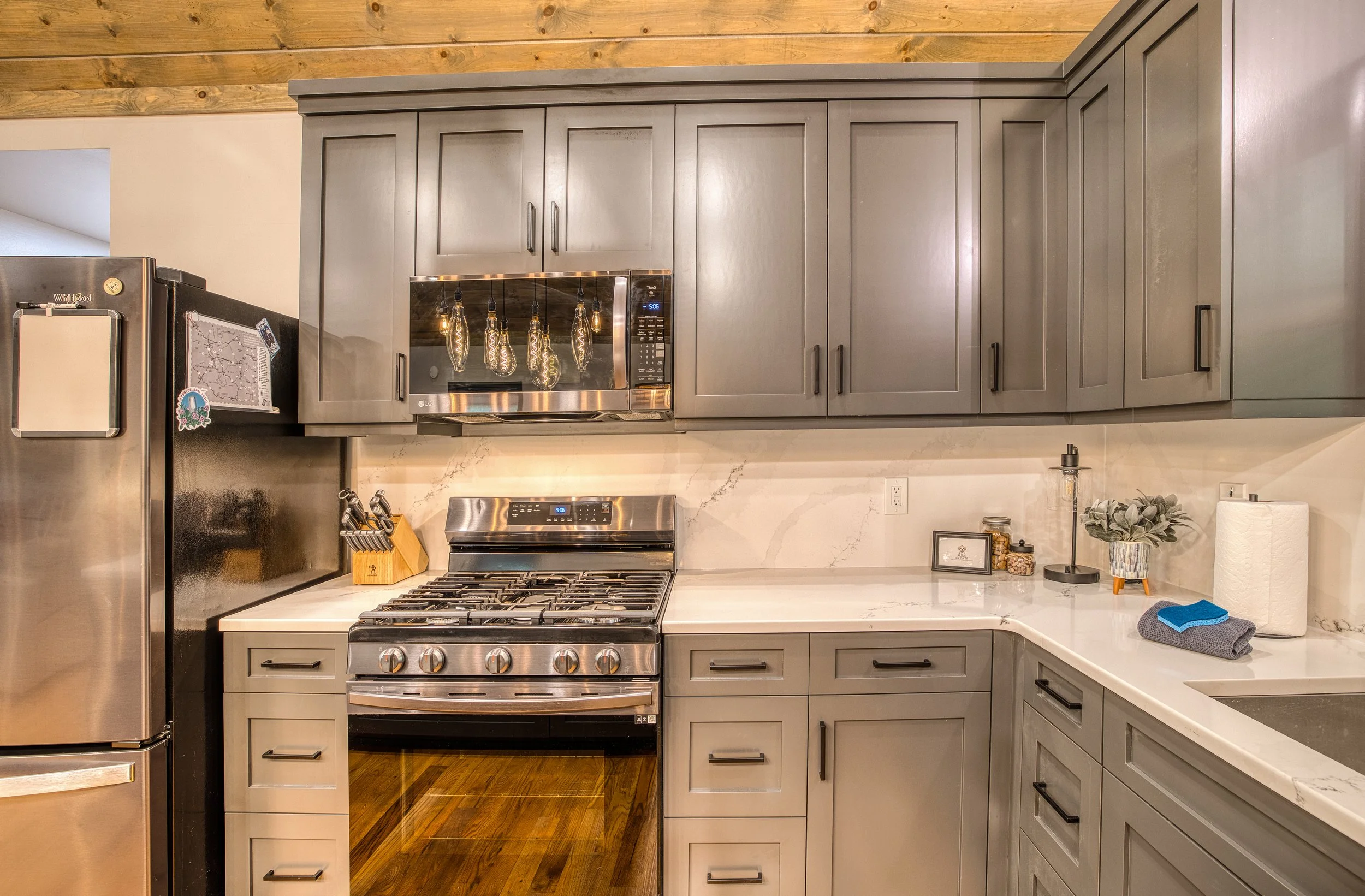 Kitchen with gas range, quartz counters, shaker cabinets, stainless appliances, and warm wood ceiling.