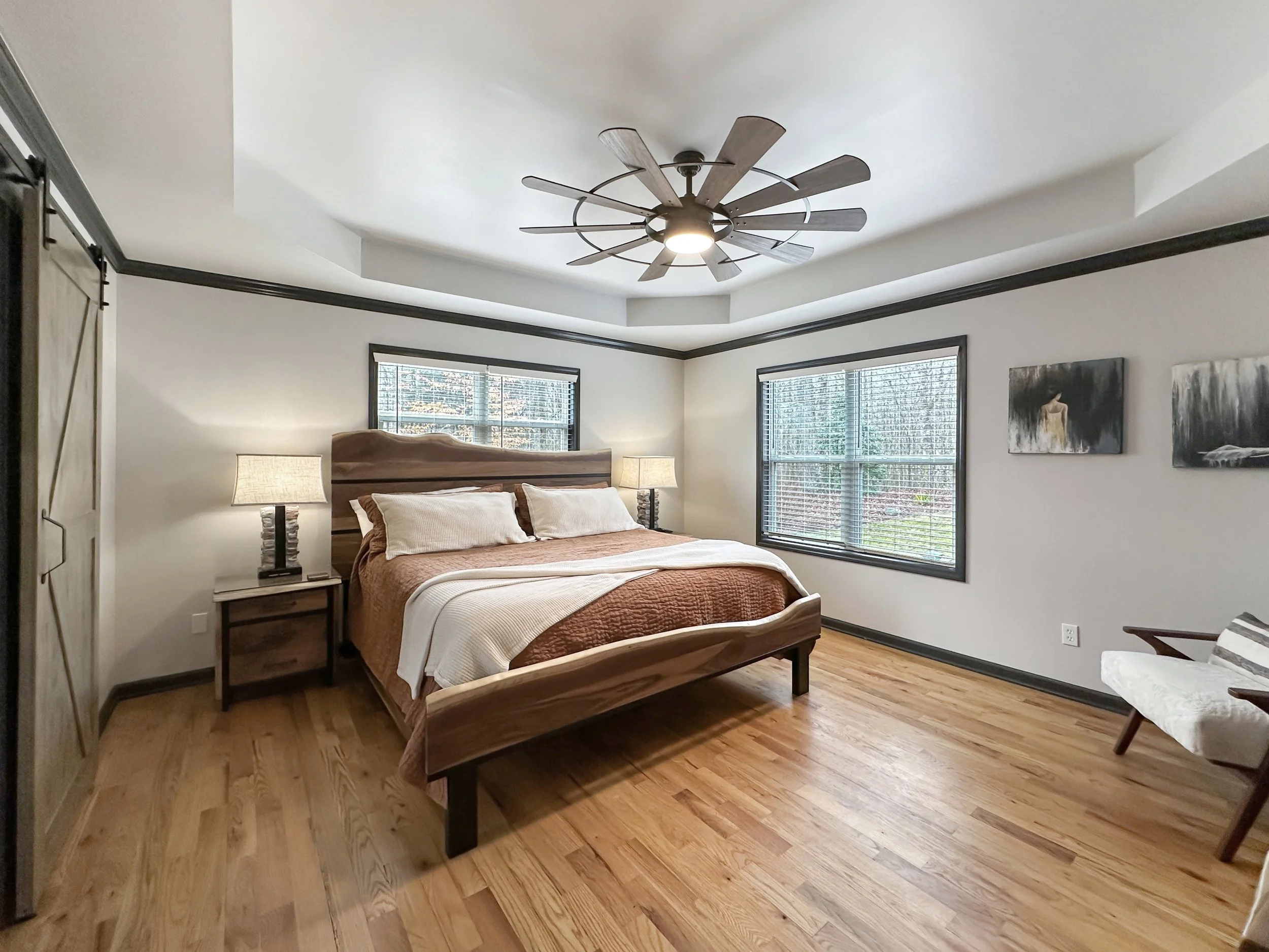 Spacious master bedroom with a luxurious king-size bed, plush linens, vaulted ceilings, and an oversized en suite bathroom. Large windows offer peaceful woodland views, creating a serene retreat for relaxation.