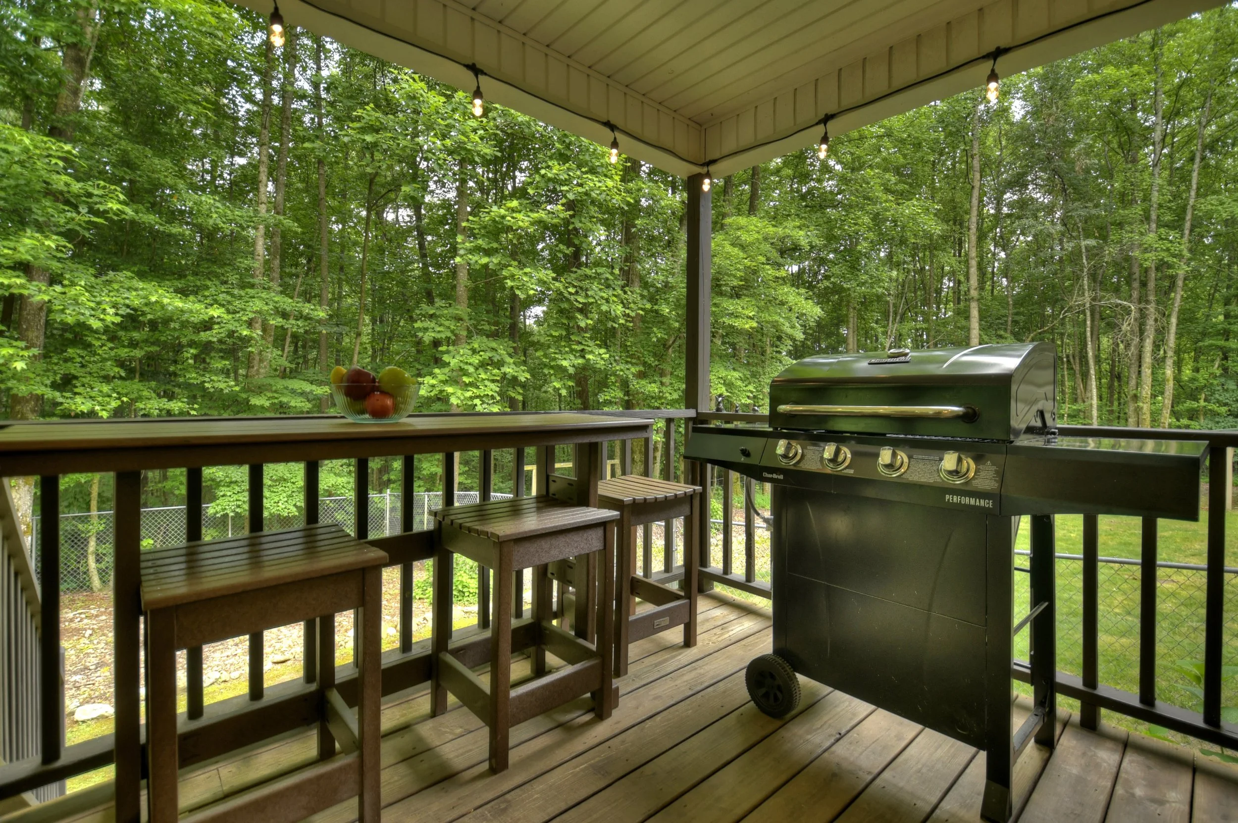 Covered back deck featuring a gas grill, outdoor dining space and seating, perfect for cooking and gathering while enjoying the serene treescape.
