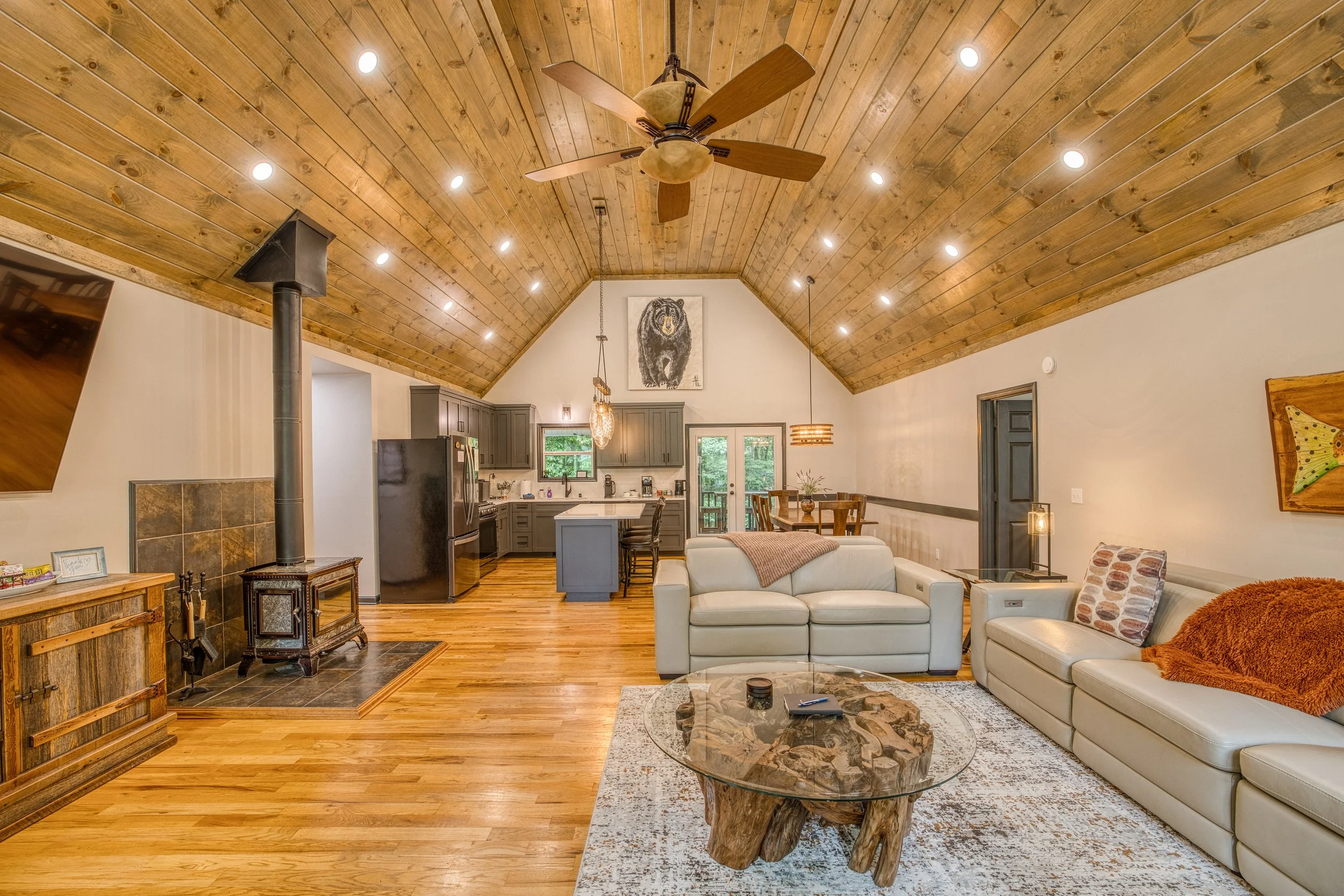 Open kitchen and living room with vaulted ceiling, kitchen island, leather sofas, and pet-friendly hardwood floors.