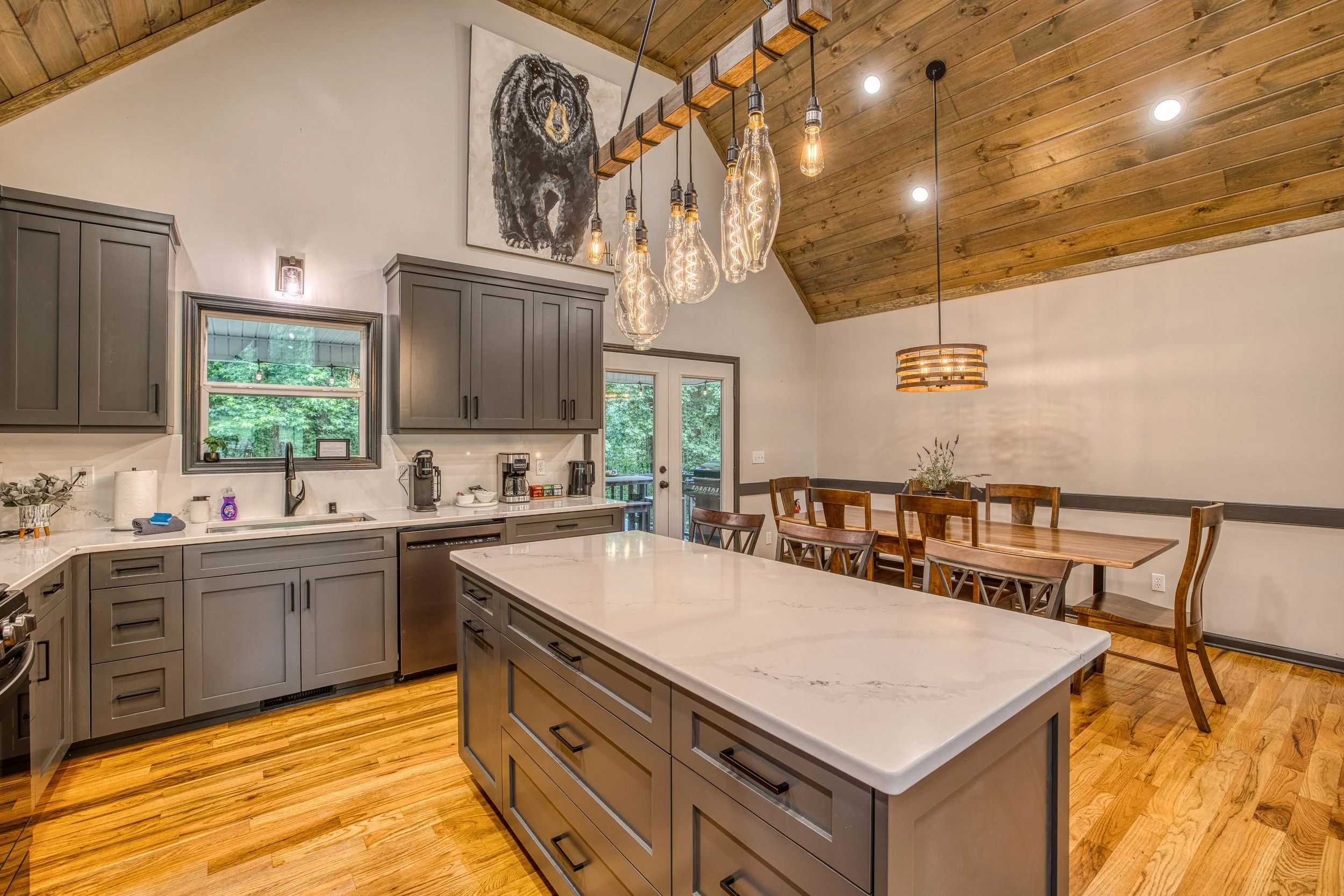 Kitchen island with quartz countertop, open concept dining for six, rustic wood table, vaulted wood ceiling.