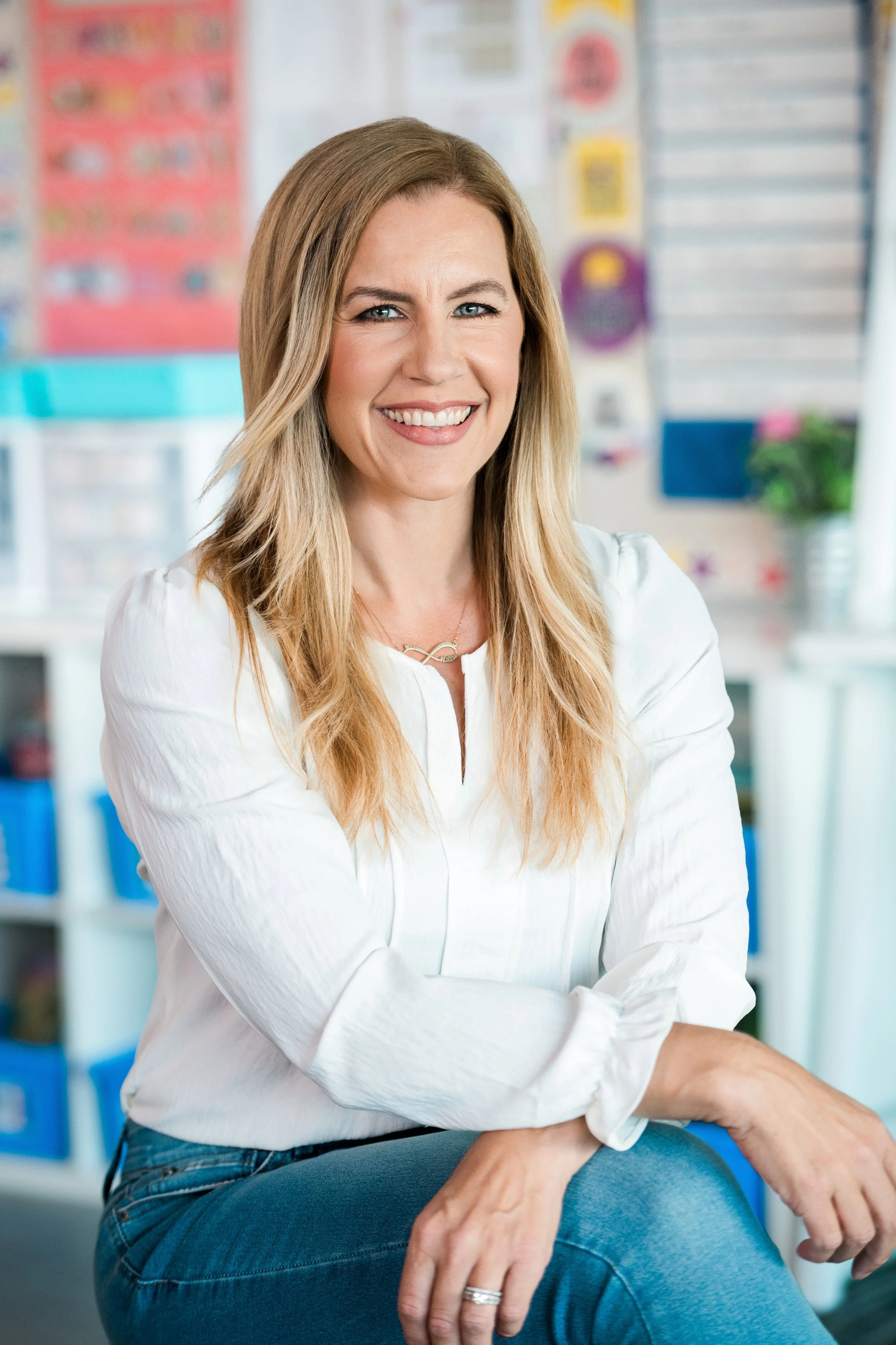 Teacher sitting in her classroom smiling at the camera.