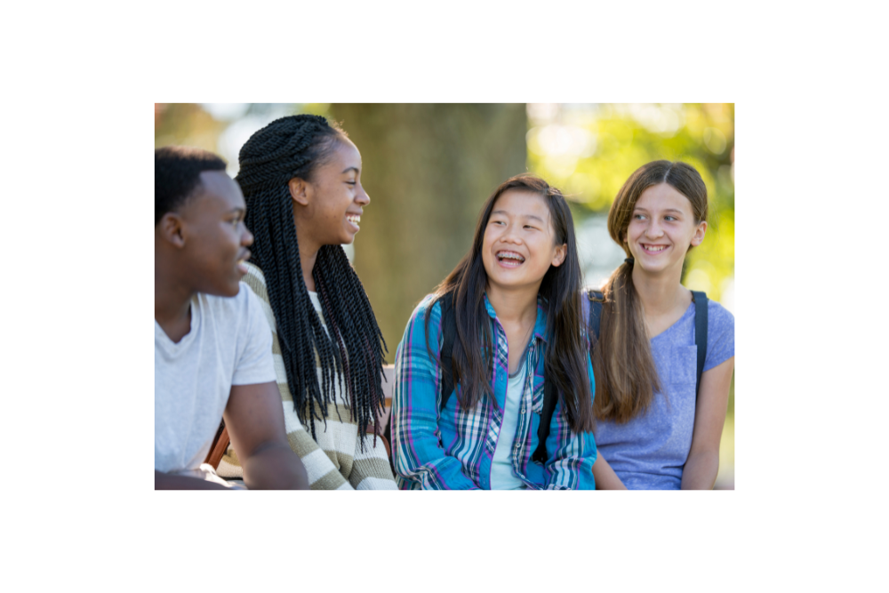 Four students sitting outside talking with each other and smiling.