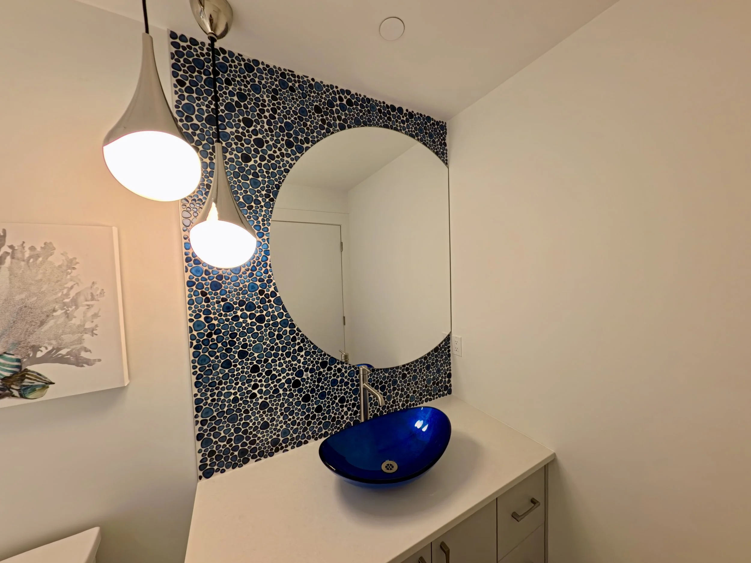 Circular custom cut mirror with river rock type tiles installed as a bathroom vanity backsplash