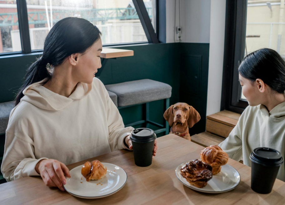 Friends enjoying breakfast at a coffee shop while their dog looks at them