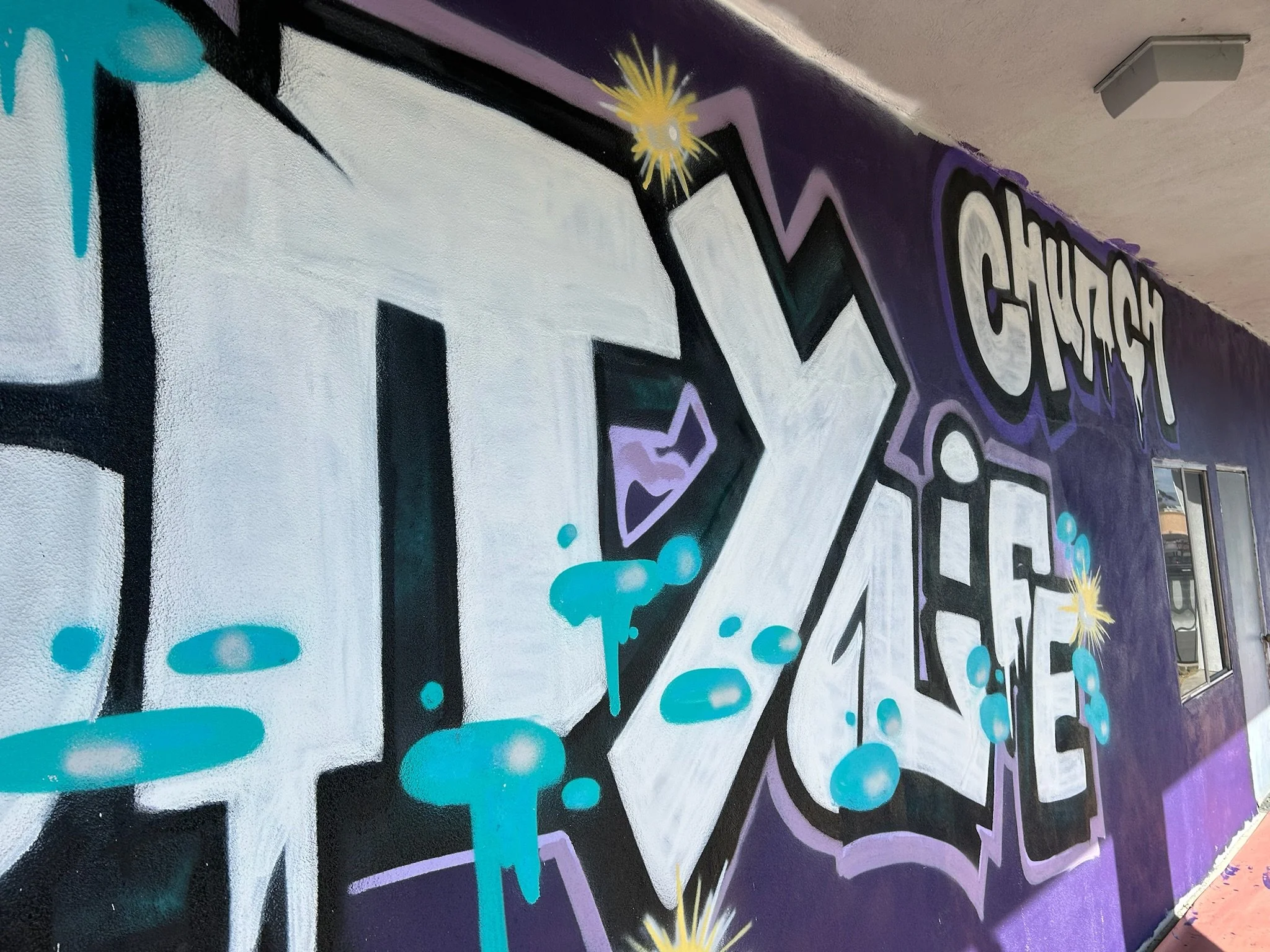 Colorful graffiti mural with the words 'Church on the' and letters 'FIX' on a purple wall, featuring black, white, purple, and light blue colors, starburst designs, and graffiti-style art.