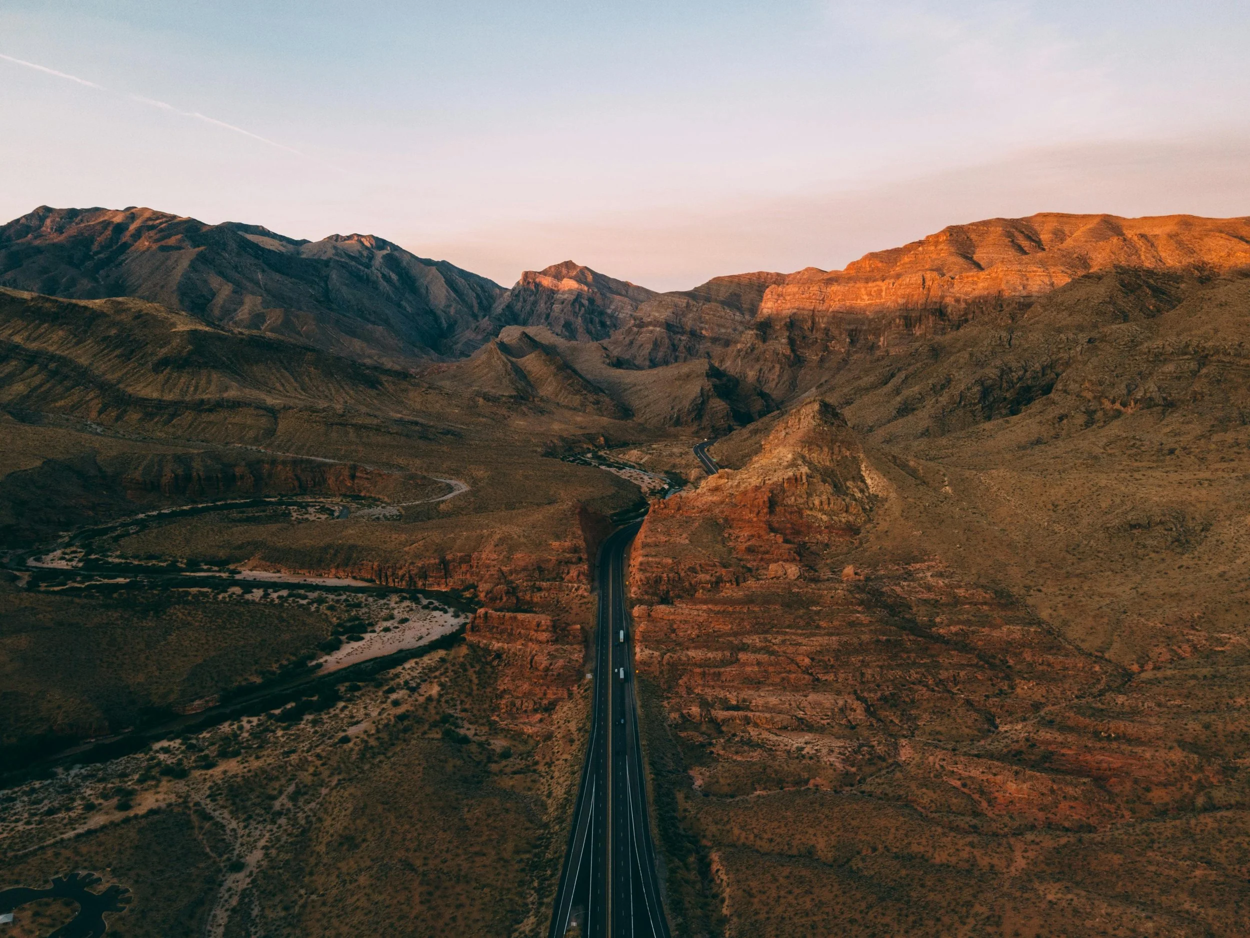 A highway running through a desert canyon with mountains in the background during sunset.