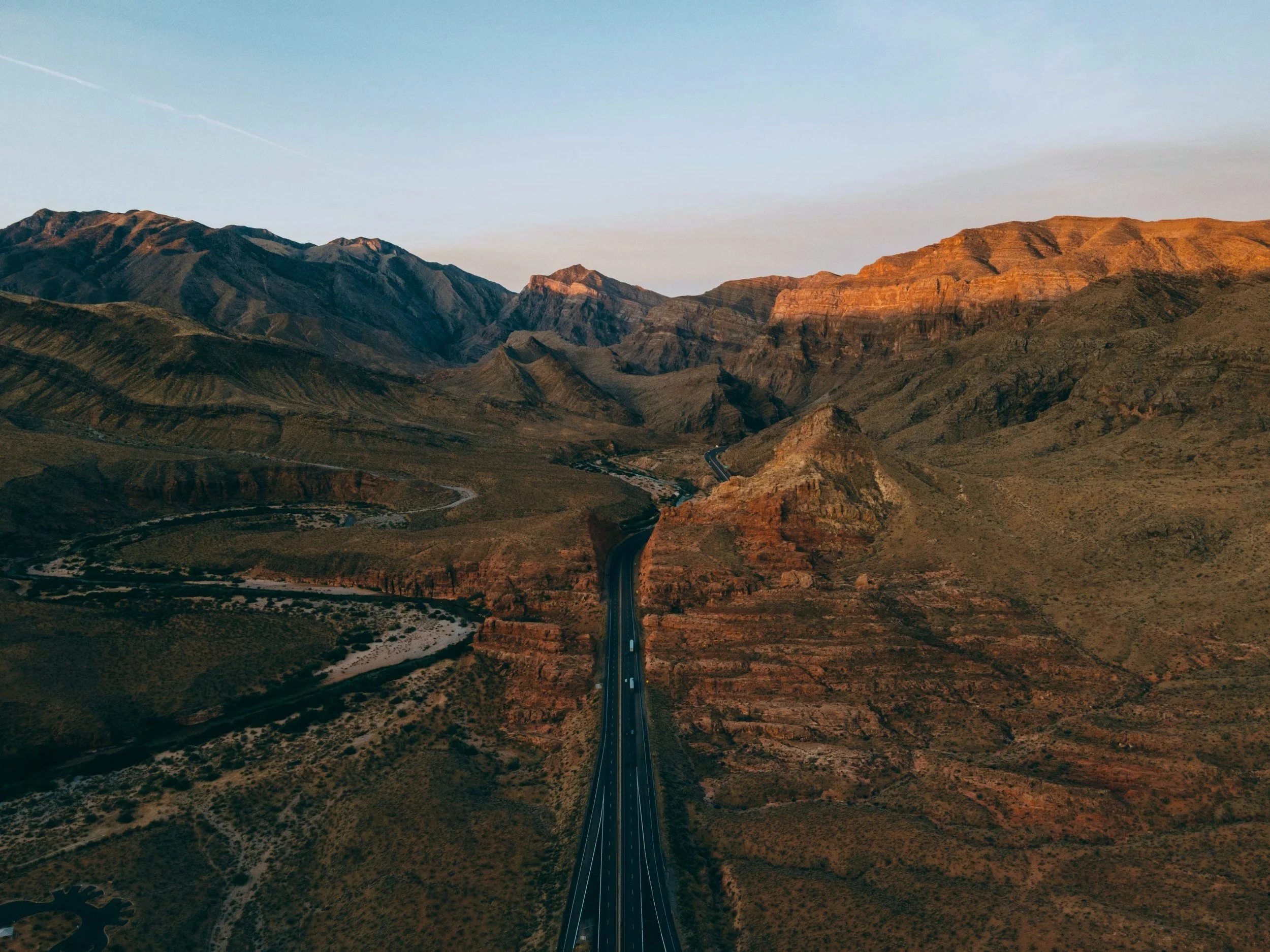 Aerial view of a highway running through a desert mountainous landscape at sunset.