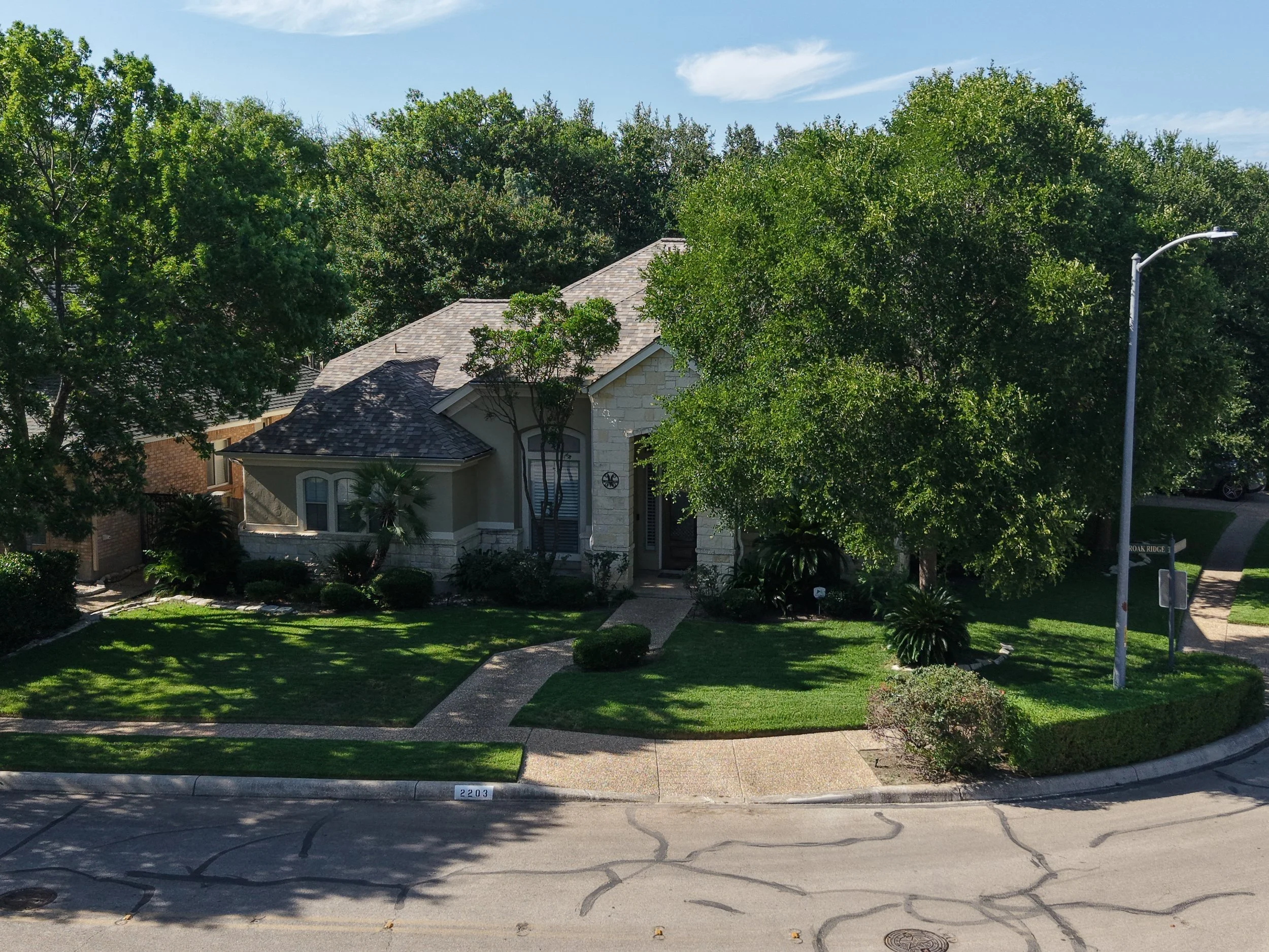 A suburban house with a well-maintained front yard, surrounded by green trees and shrubbery, on a sunny day.