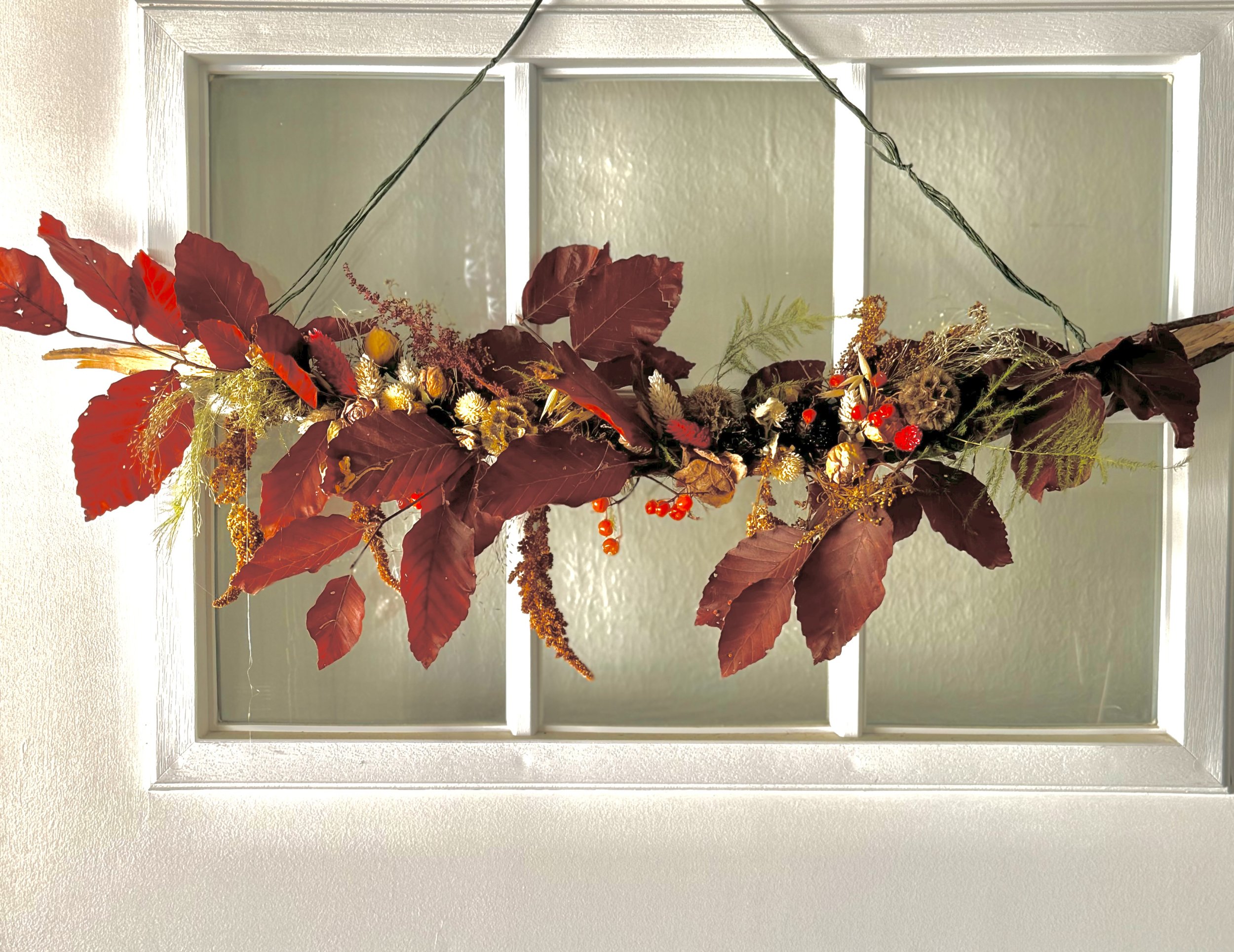 Autumn-themed wreath with red leaves and decorative elements on a window frame.