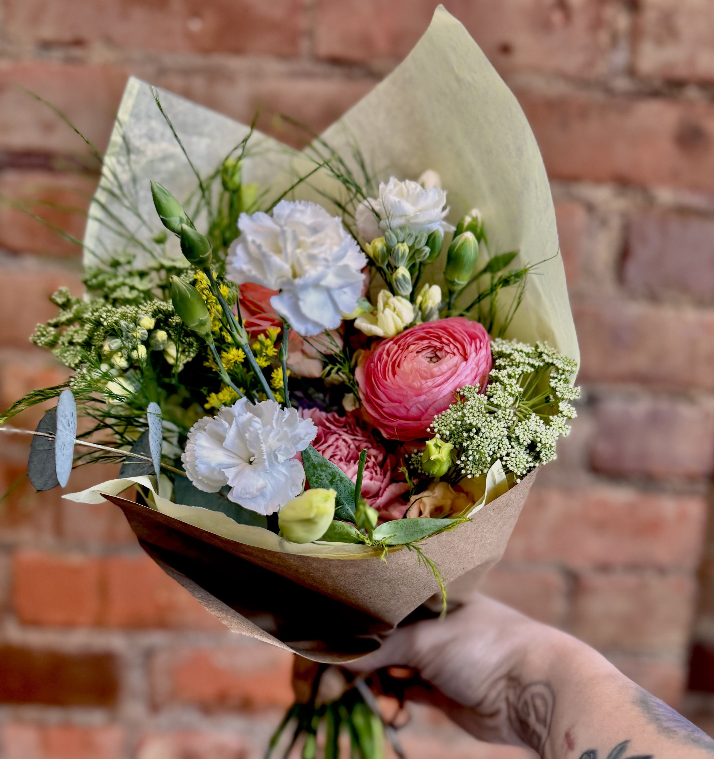 Bouquet of mixed flowers with pink ranunculus and white carnations against brick wall background