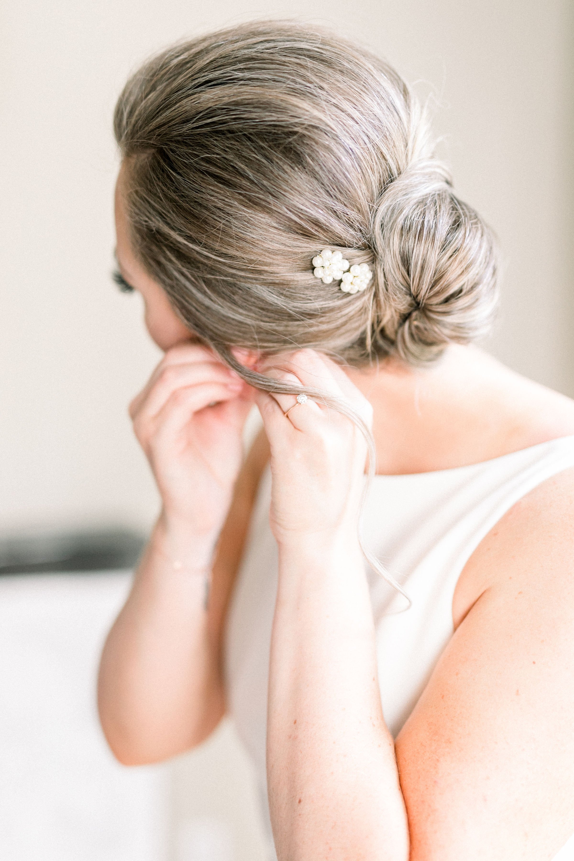 Woman adjusting earring with elegant updo hairstyle and floral hair accessory.