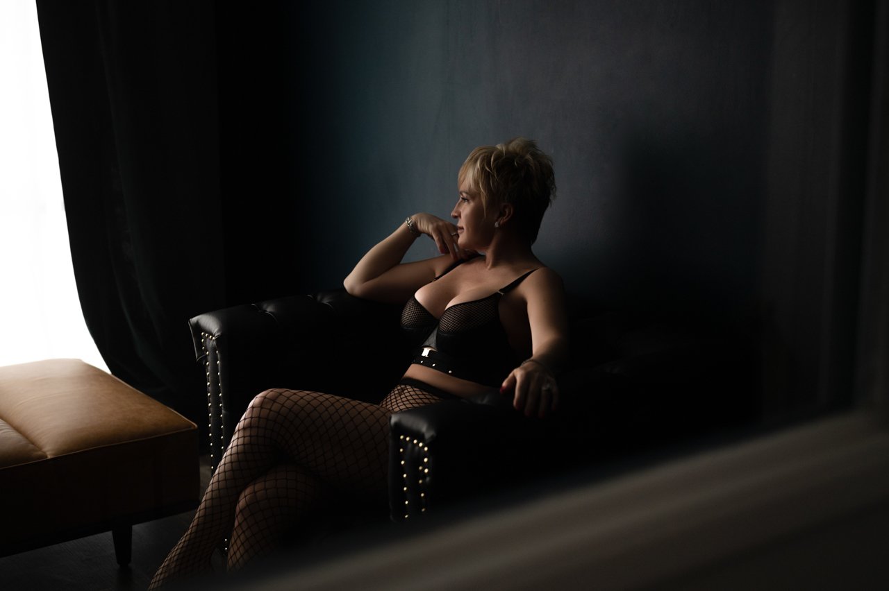 Person in fishnet outfit sitting on black sofa in dimly lit room.