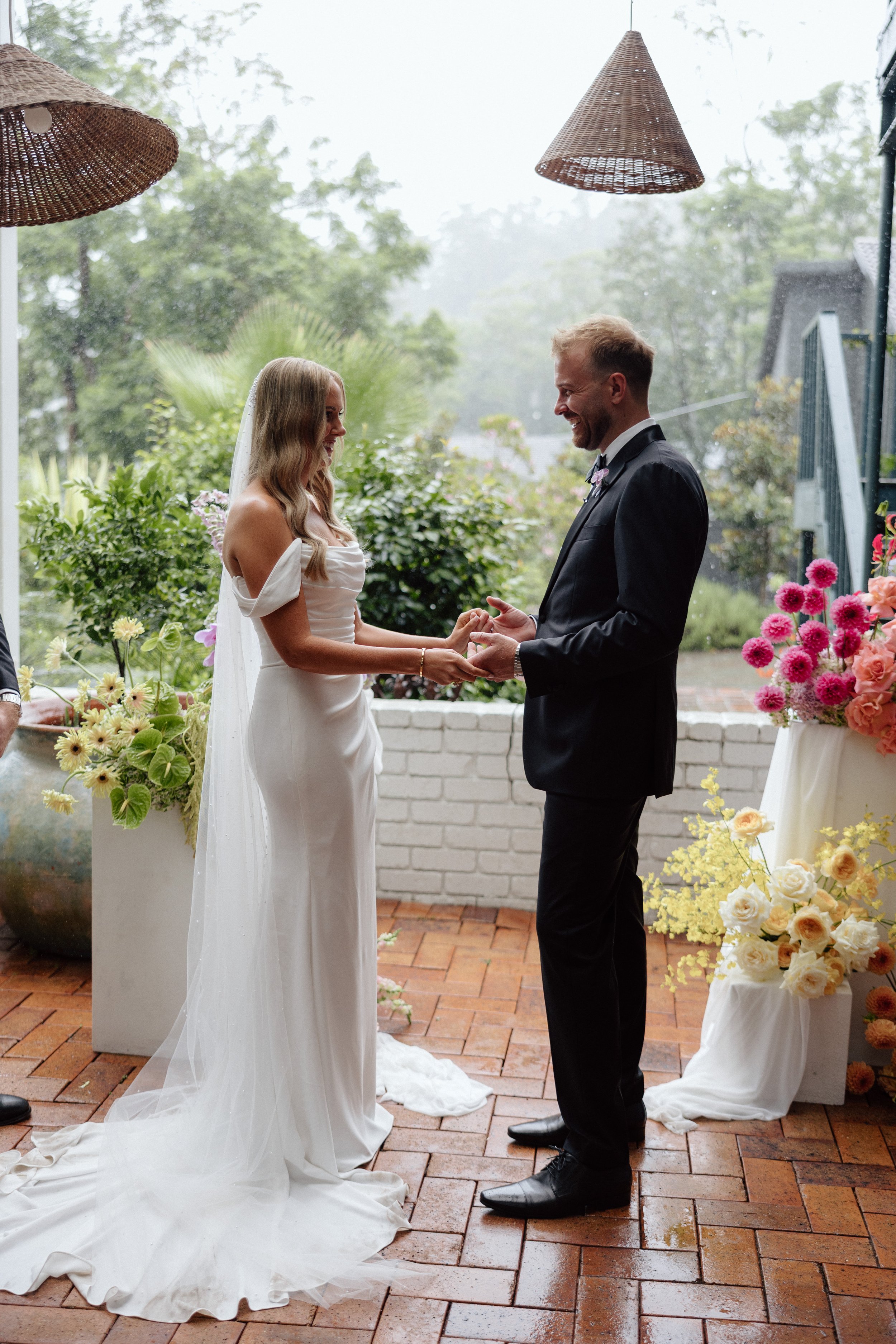 Black and white photo of a bride and groom kissing outdoors at their wedding, surrounded by floral arrangements.