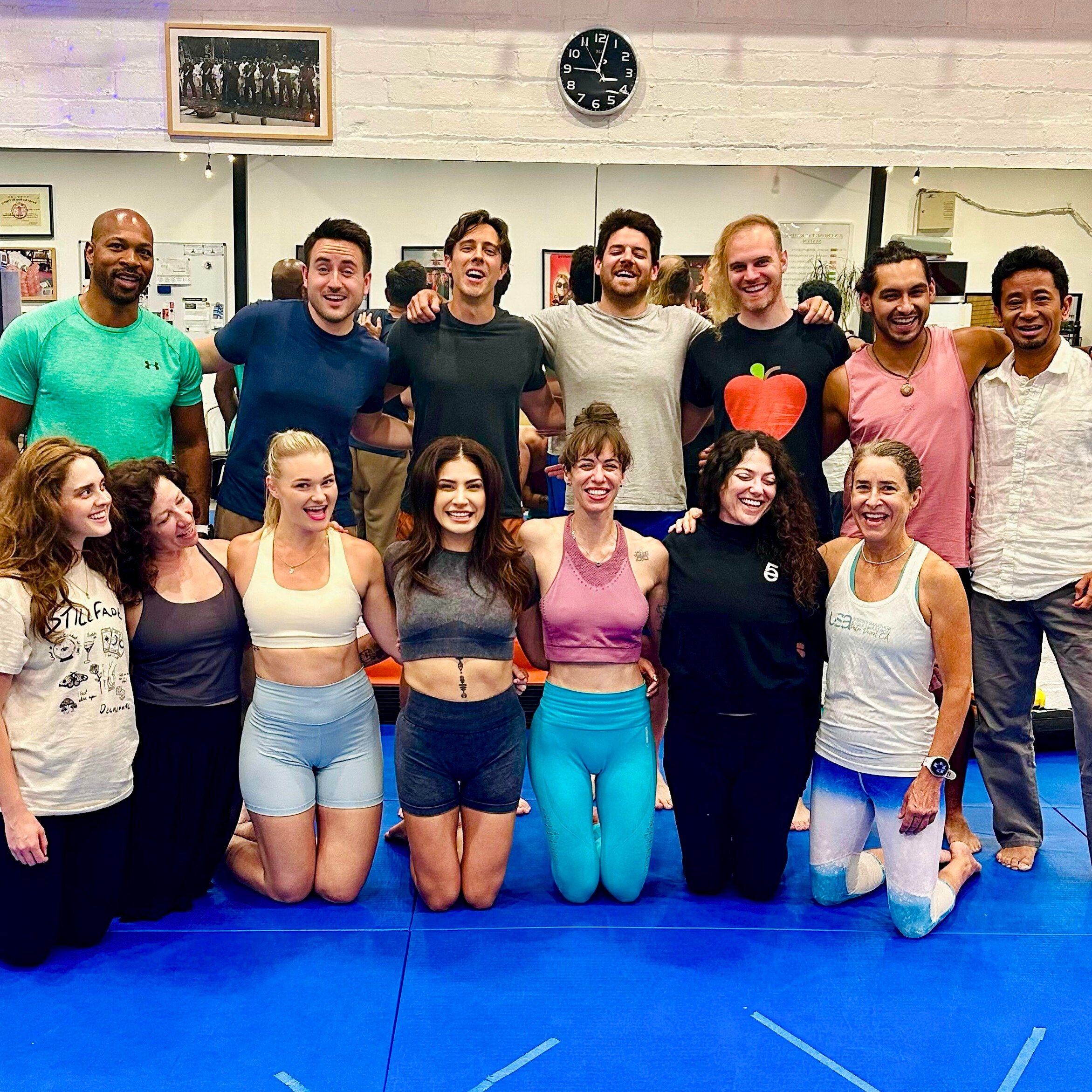 Group of people posing together in a gym or dance studio, smiling and celebrating after a workout or dance class.