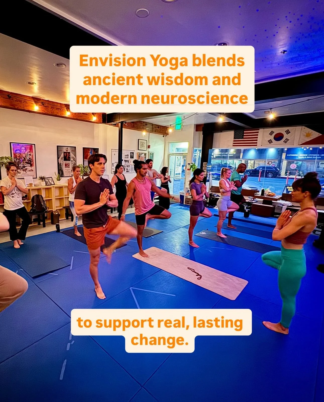 A woman with wavy hair stands on a balcony during sunset, looking to the camera with a serious expression. There are residential buildings and trees in the background.