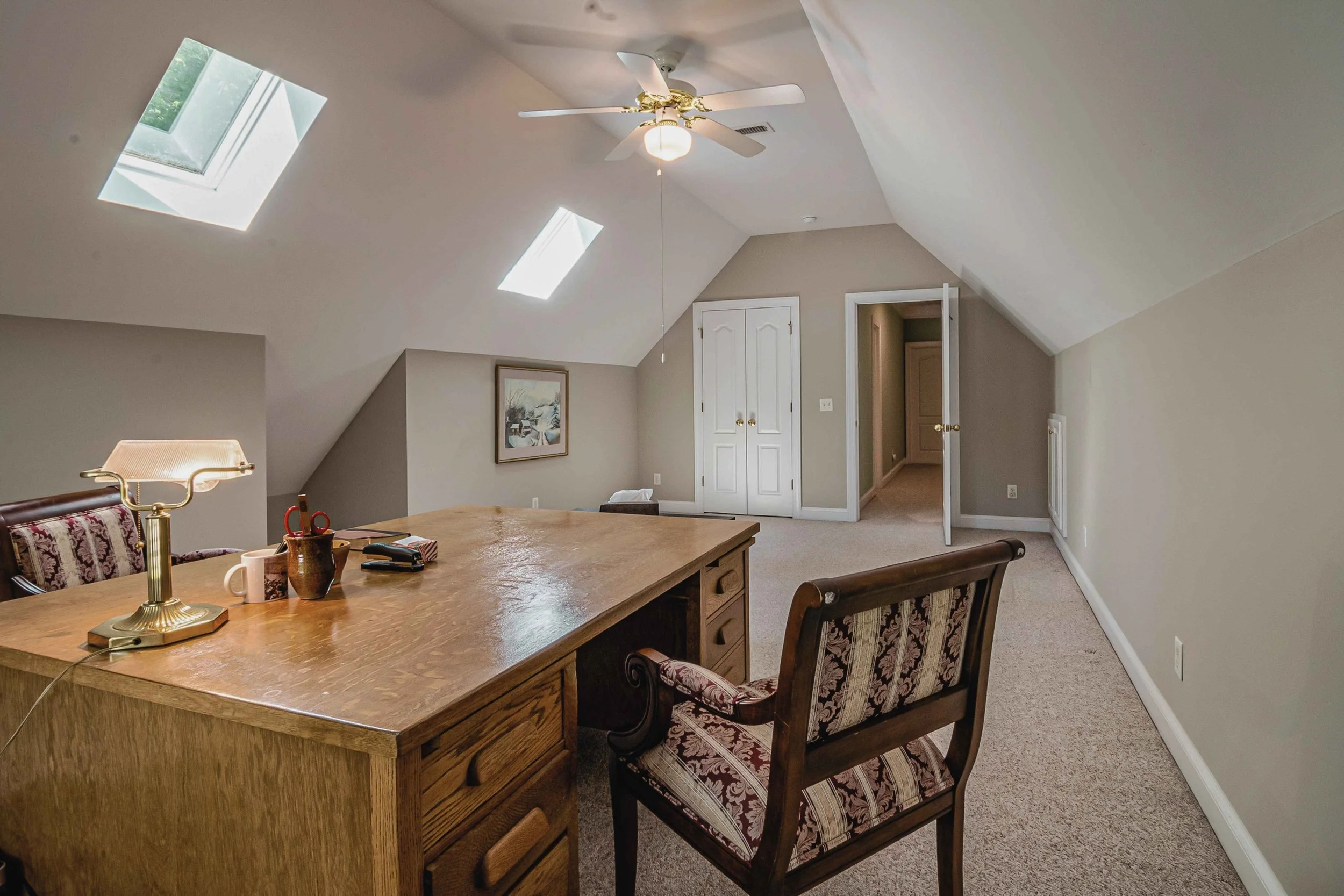 Finished attic room with sloped ceilings, two skylights, a desk, and a closet with double doors.