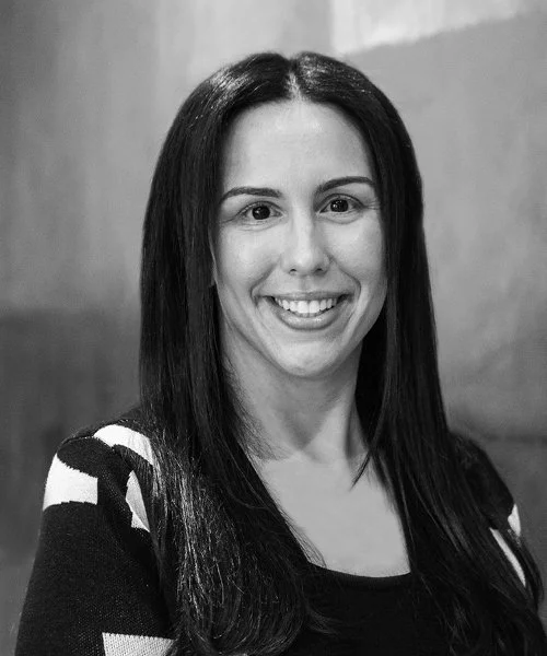 Black and white photo of a woman with long straight hair smiling, wearing a patterned sweater.