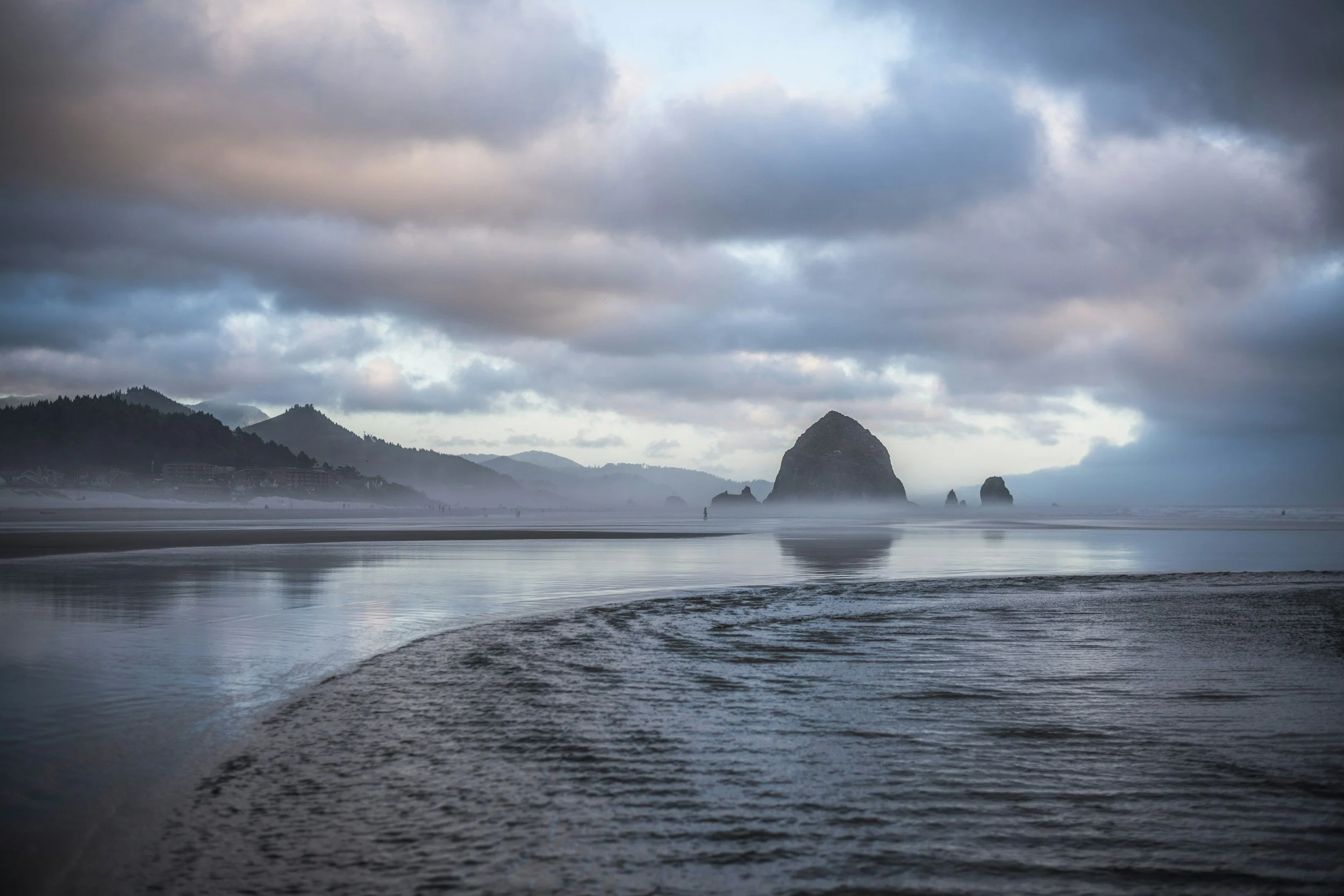 Coastal landscape with Haystack Rock and cloudy sky at sunset