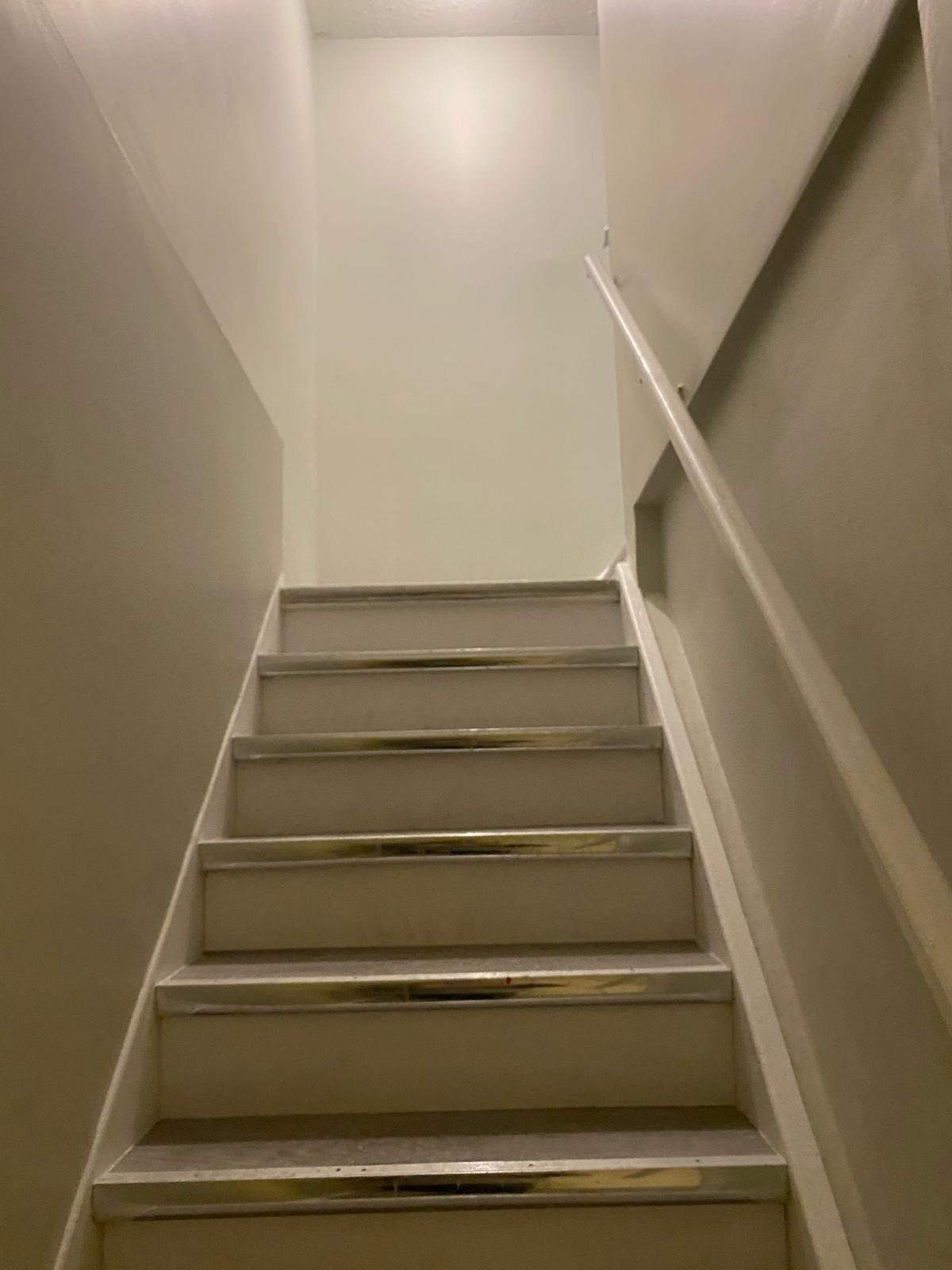 A staircase with six steps, metal edges, and a handrail on the right side, leading up to a white wall and ceiling.