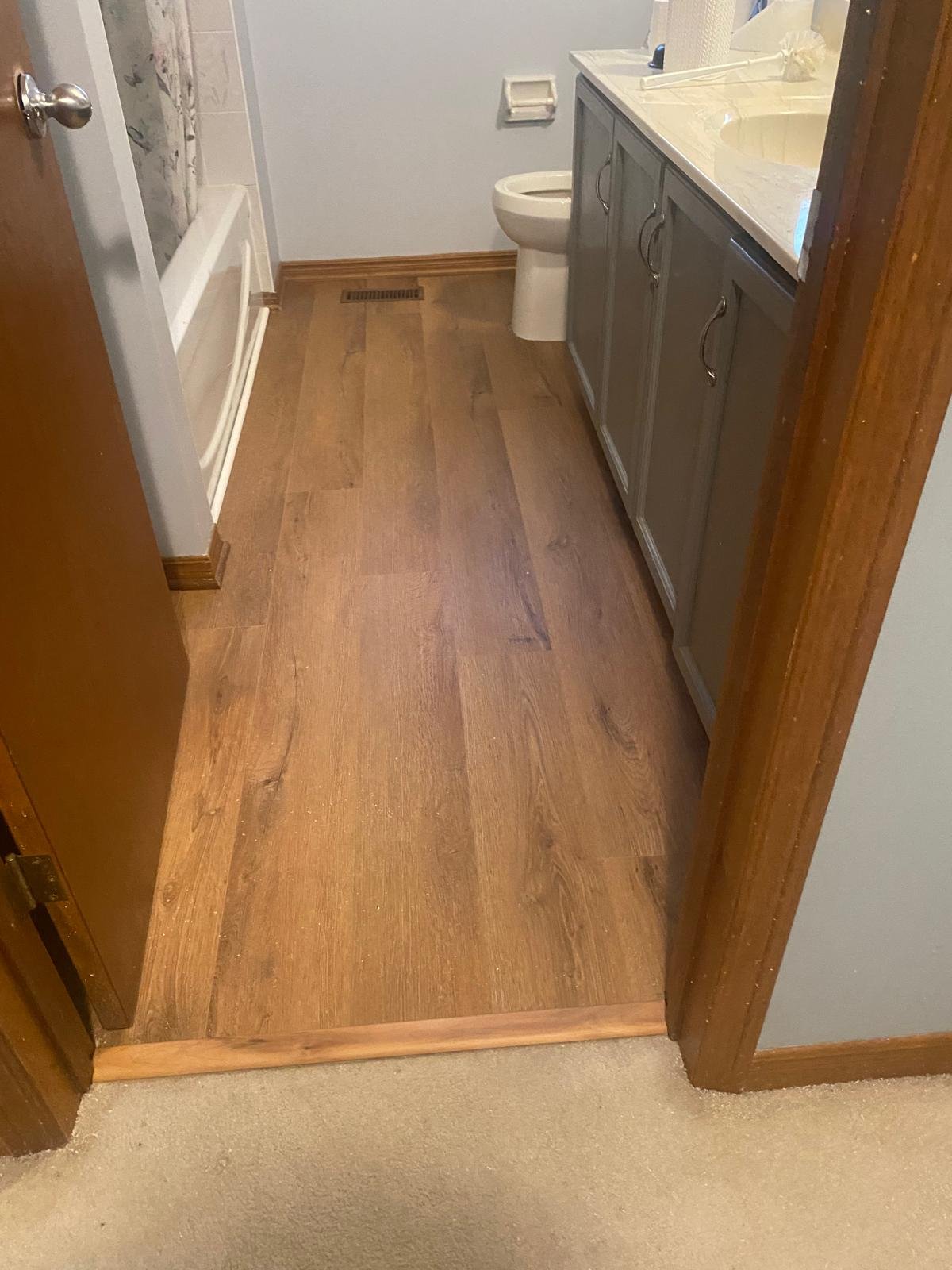 Bathroom with wood flooring, a toilet, a gray vanity with a cream-colored countertop, and a bathtub with a floral shower curtain.