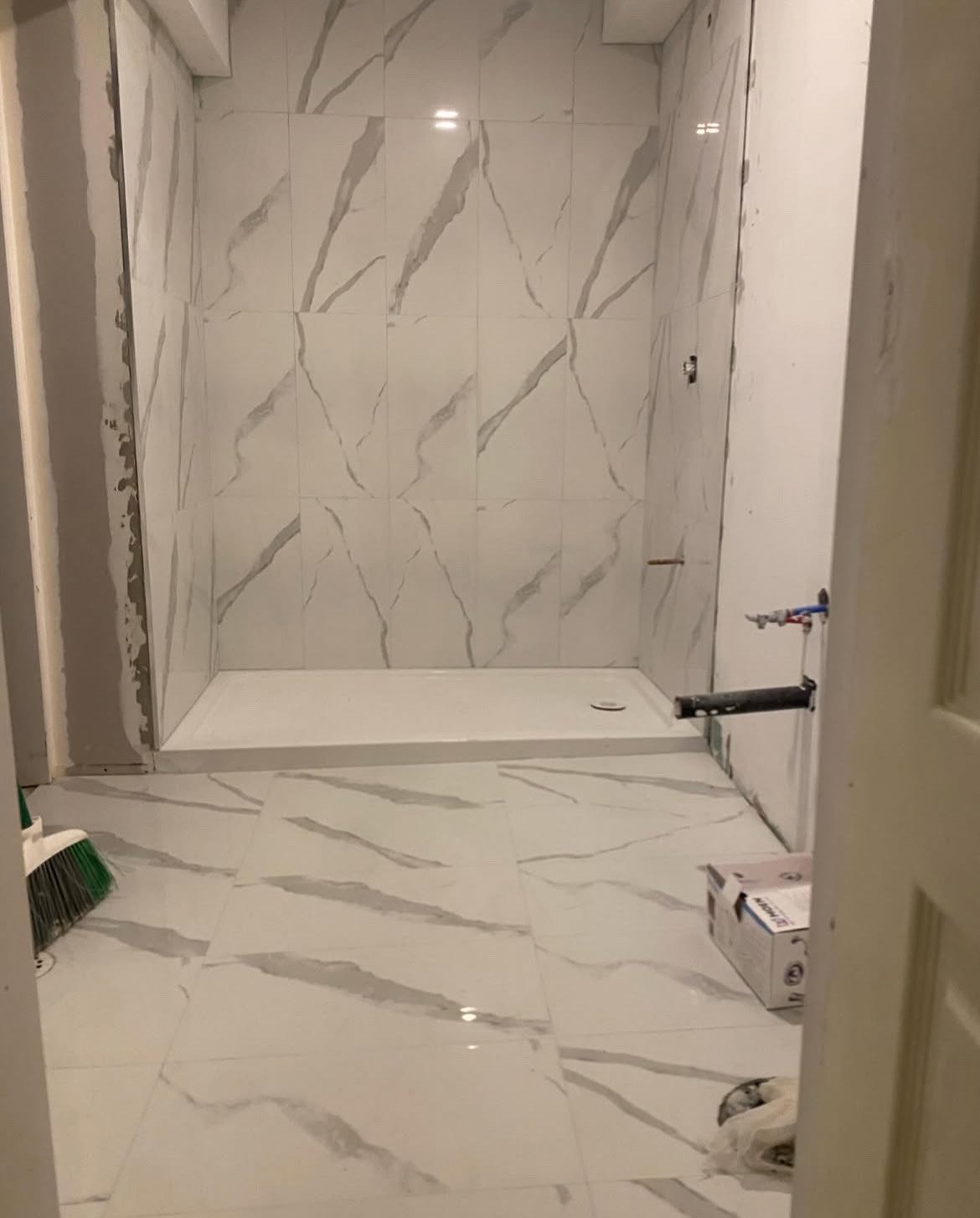 Under construction bathroom with marble tiles on floor and walls, shower area in the background, and construction tools and materials present.