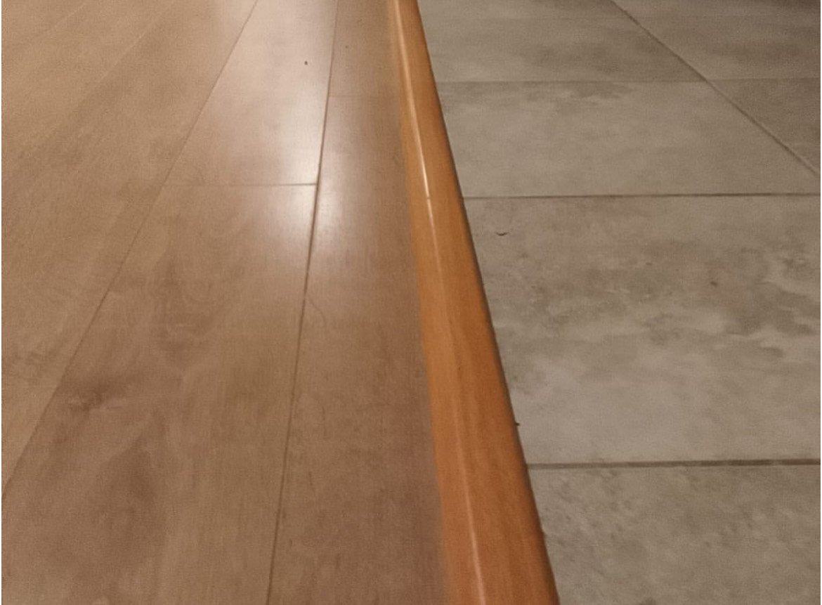 Close-up of a wooden transition strip between two types of flooring, one hardwood and one tile.
