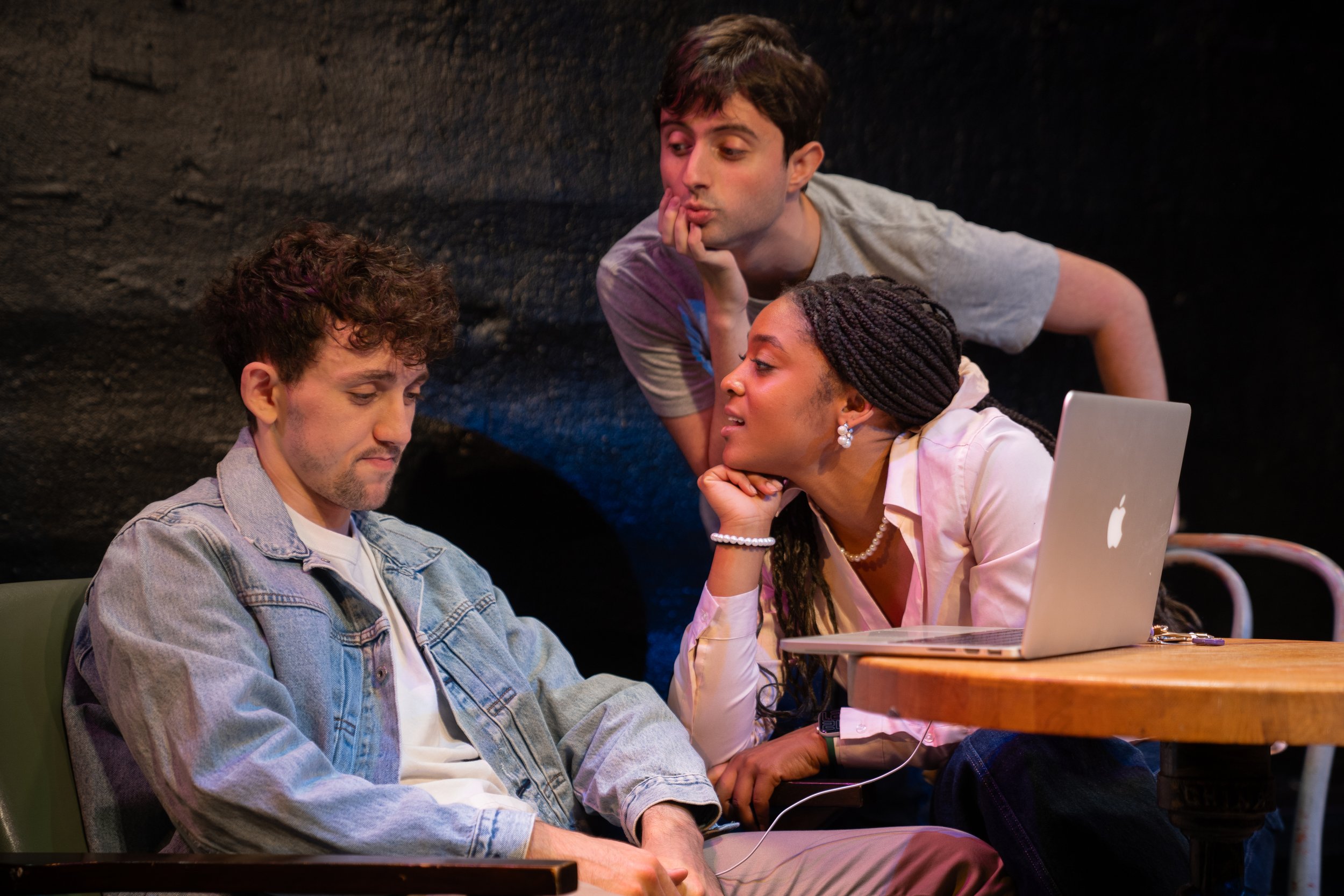 Remidy Destyn Dixon in "In Chief" - Three young adults gathered around a table, with one sitting and two leaning over, having a serious or thoughtful discussion. A laptop is on the table.