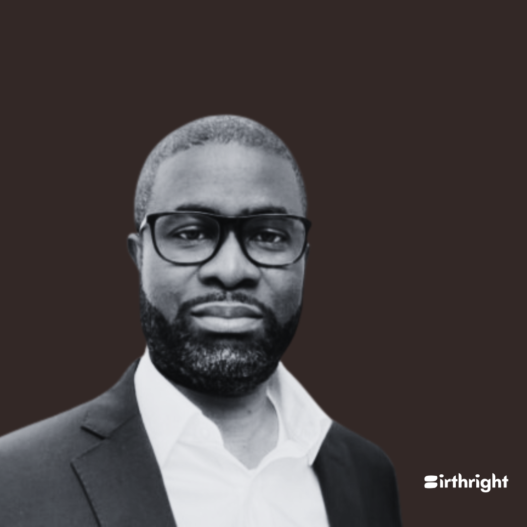 Black and white portrait of a man with a beard and glasses wearing a suit and white shirt against a dark background.