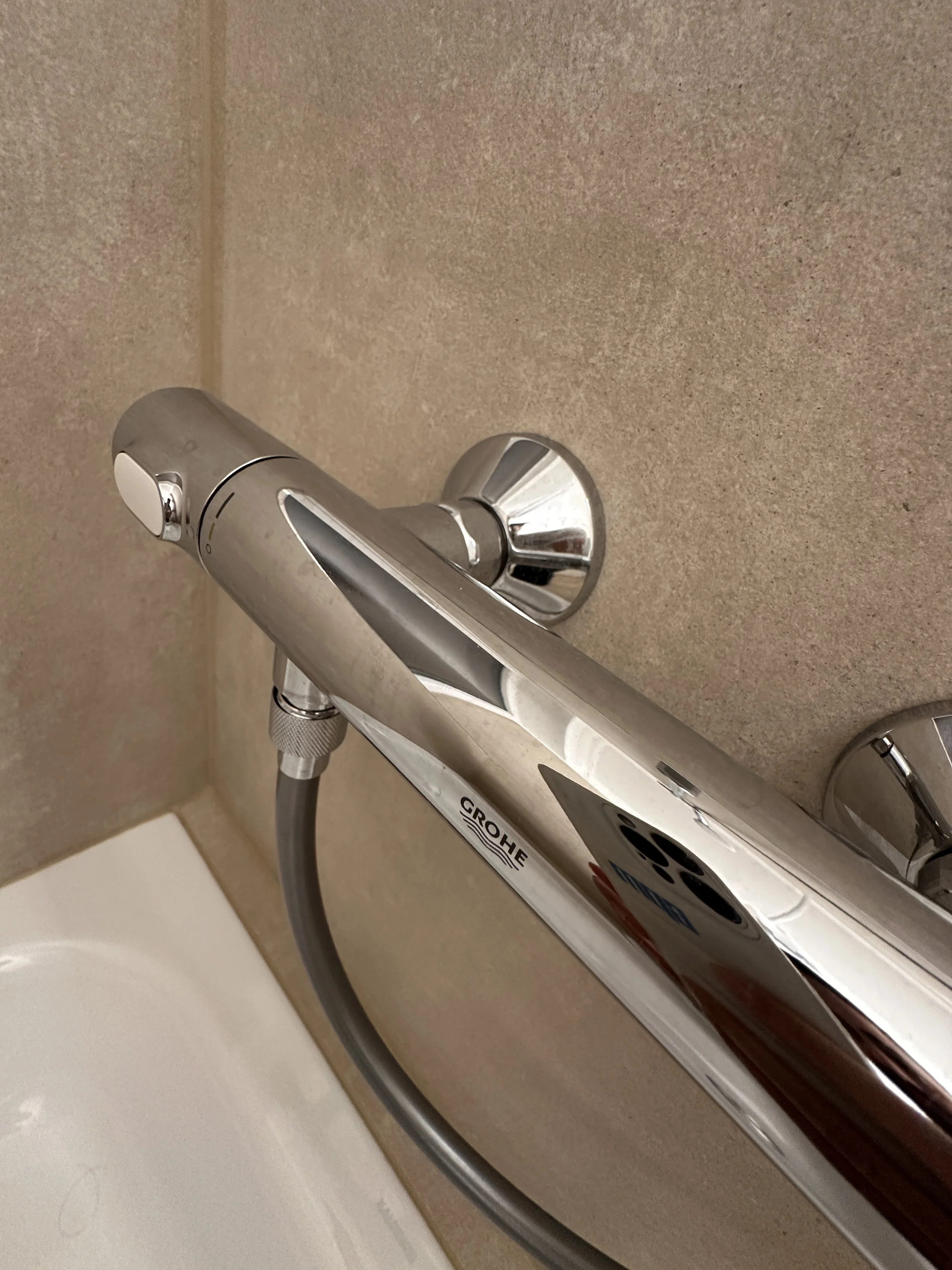 Nahaufnahme eines modernen, silbernen Duscharmatur mit Schlauch an einer beige Wand.