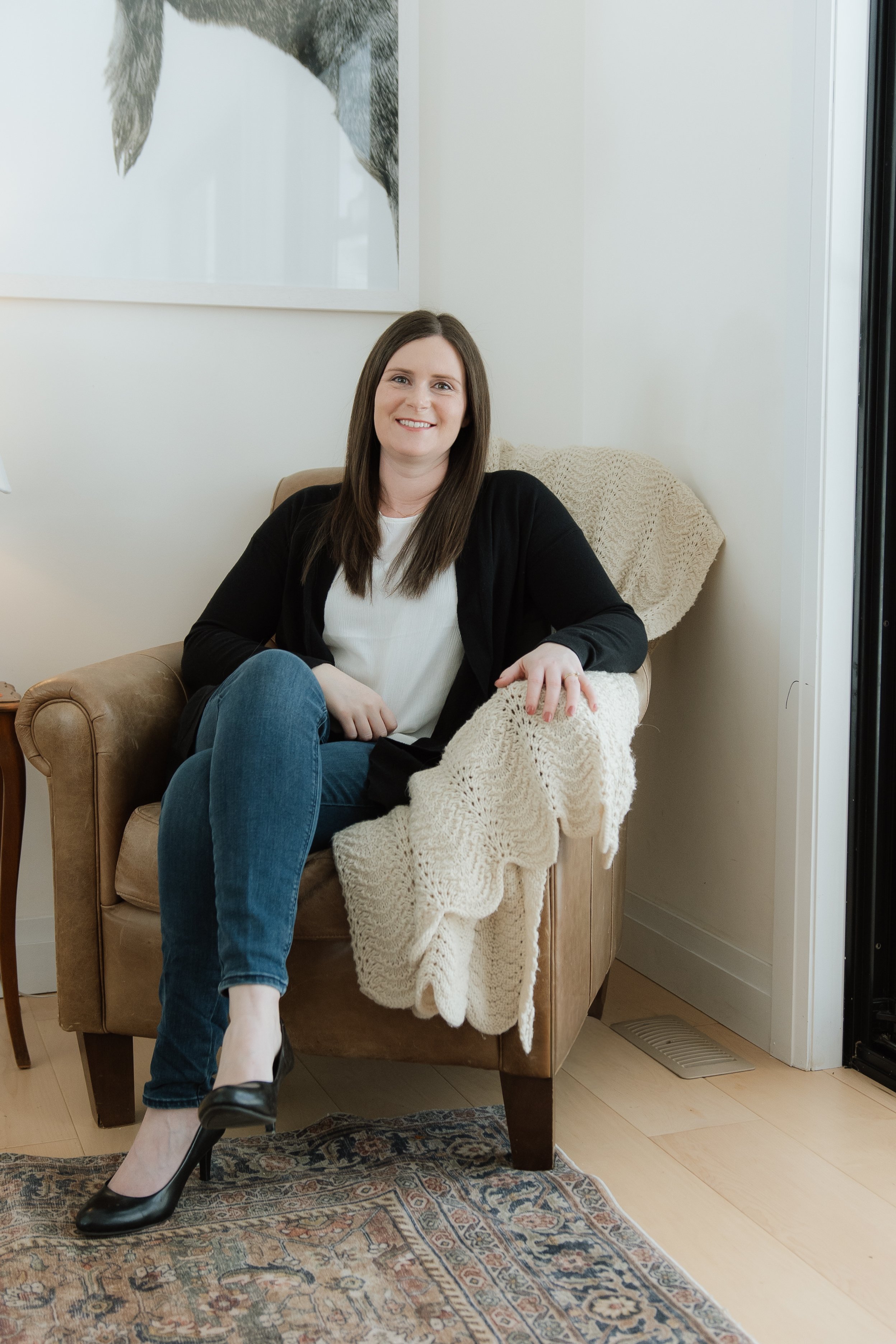 A photo of Rachelle Stephens, owner of Rachelle Stephens Counselling & Consulting - a woman with long brown hair sitting on a tan armchair, smiling at the camera.