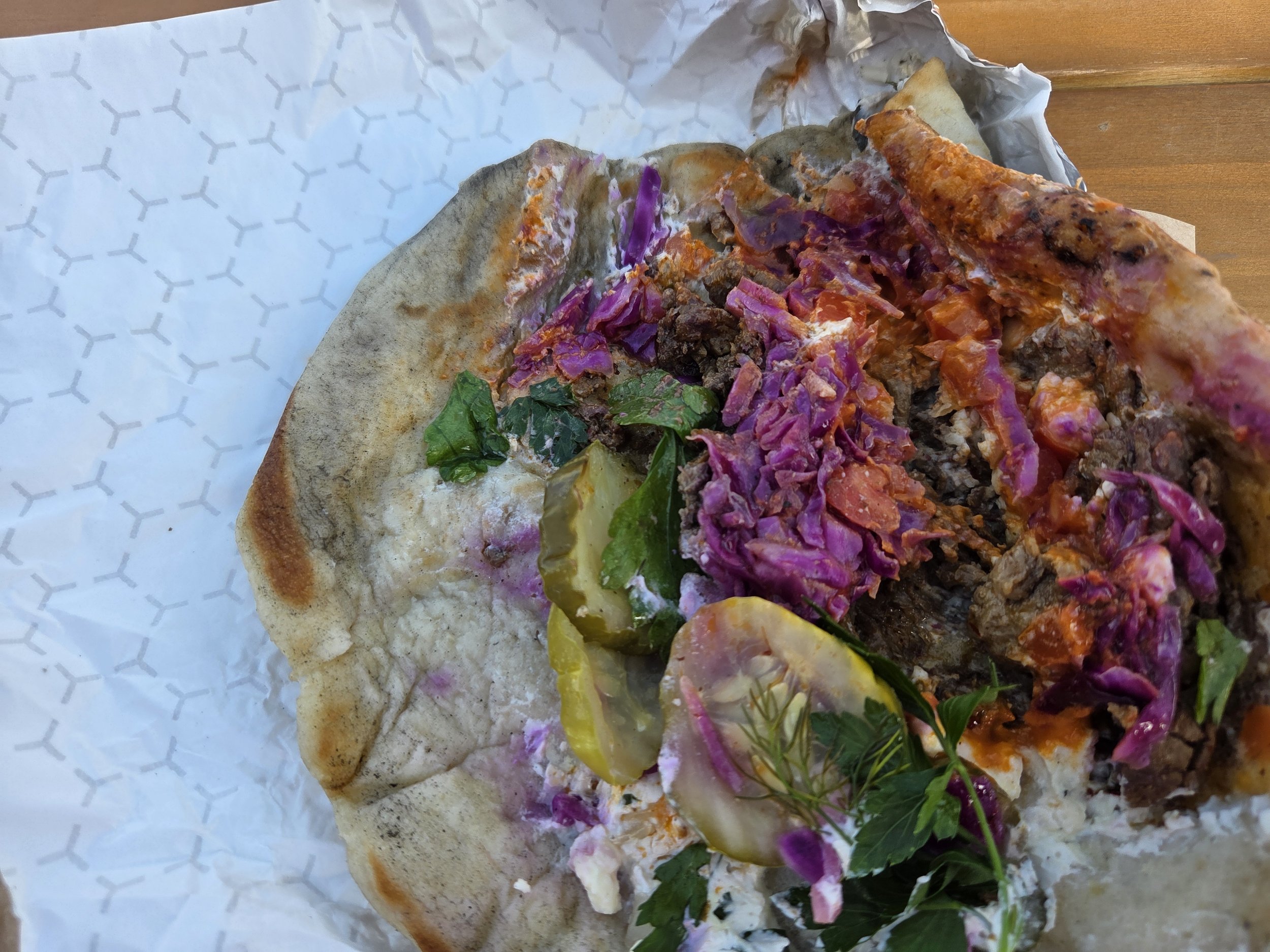 Partial views of a pita with vegetables and meat on a paper-lined tray.