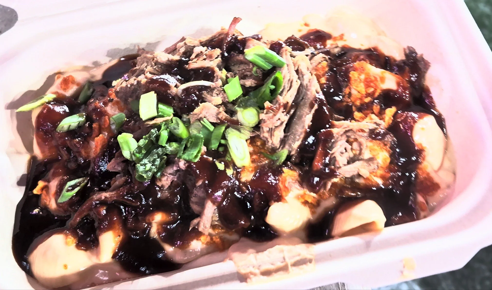Mac and cheese topped with shredded meat, green onions, and sauce in a tray.