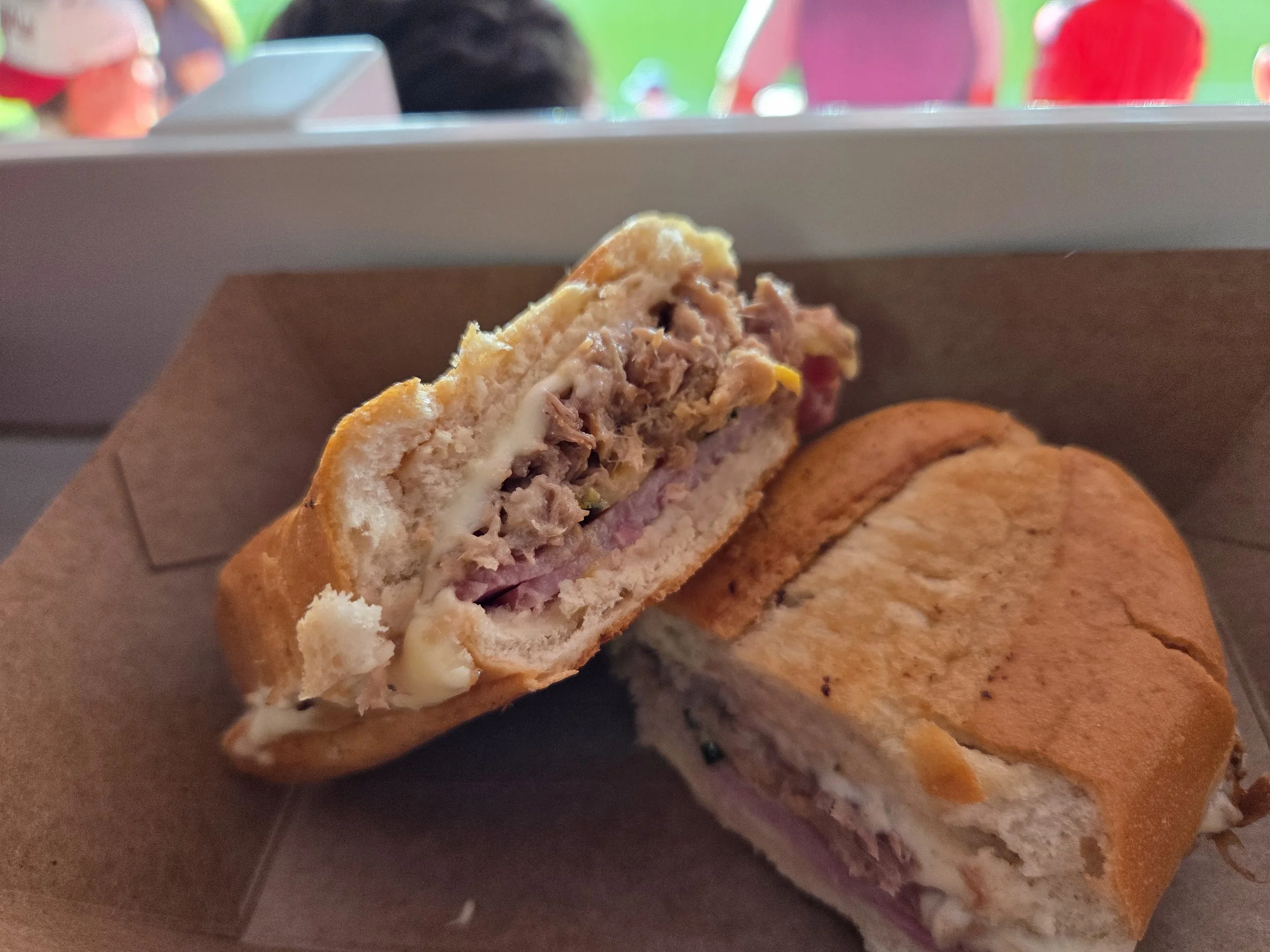 Close-up of a half-eaten sandwich with layers of meat, cheese, and vegetables in a toasted bun, resting on a brown paper tray.
