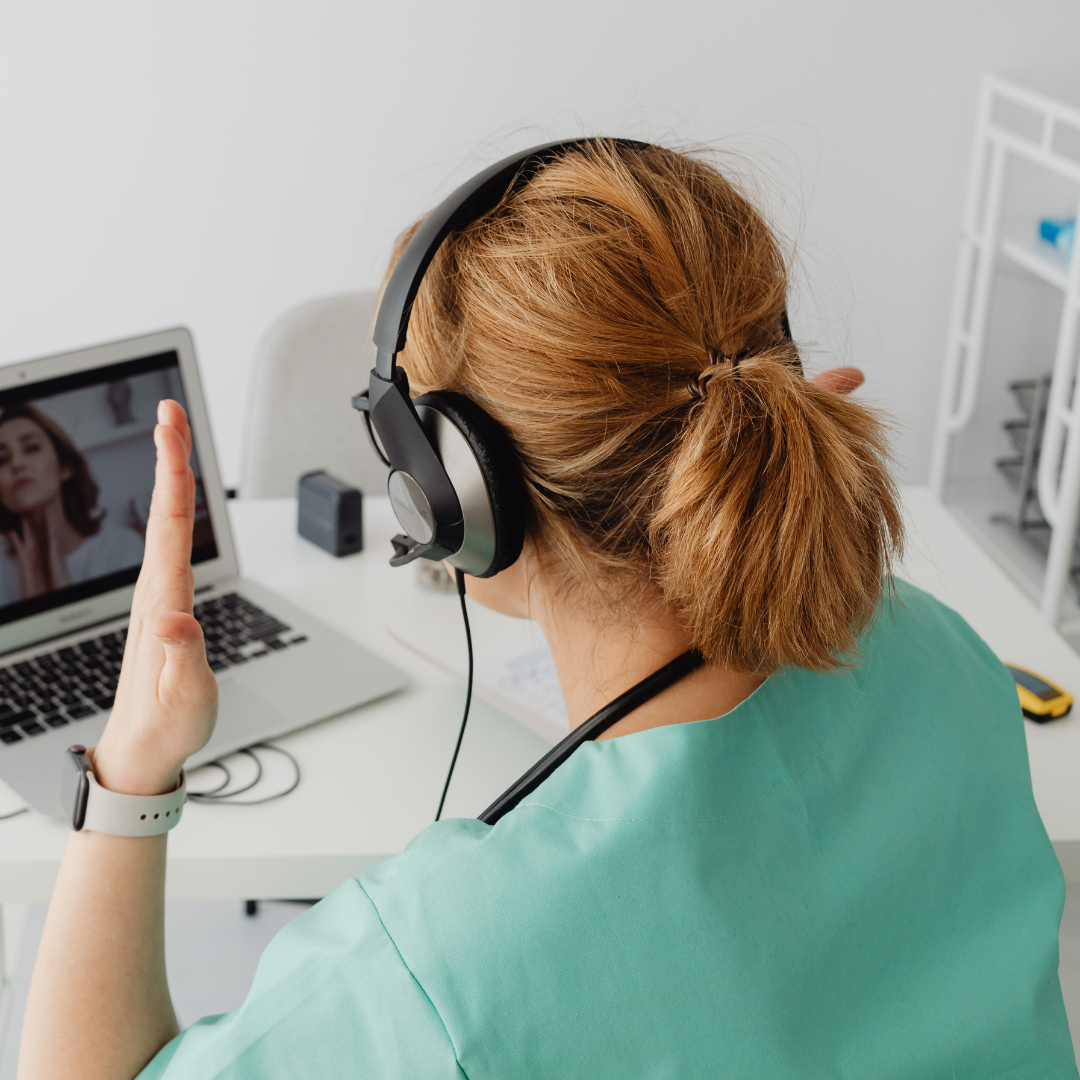 Medical professional wearing headphones during a virtual consultation on a laptop.