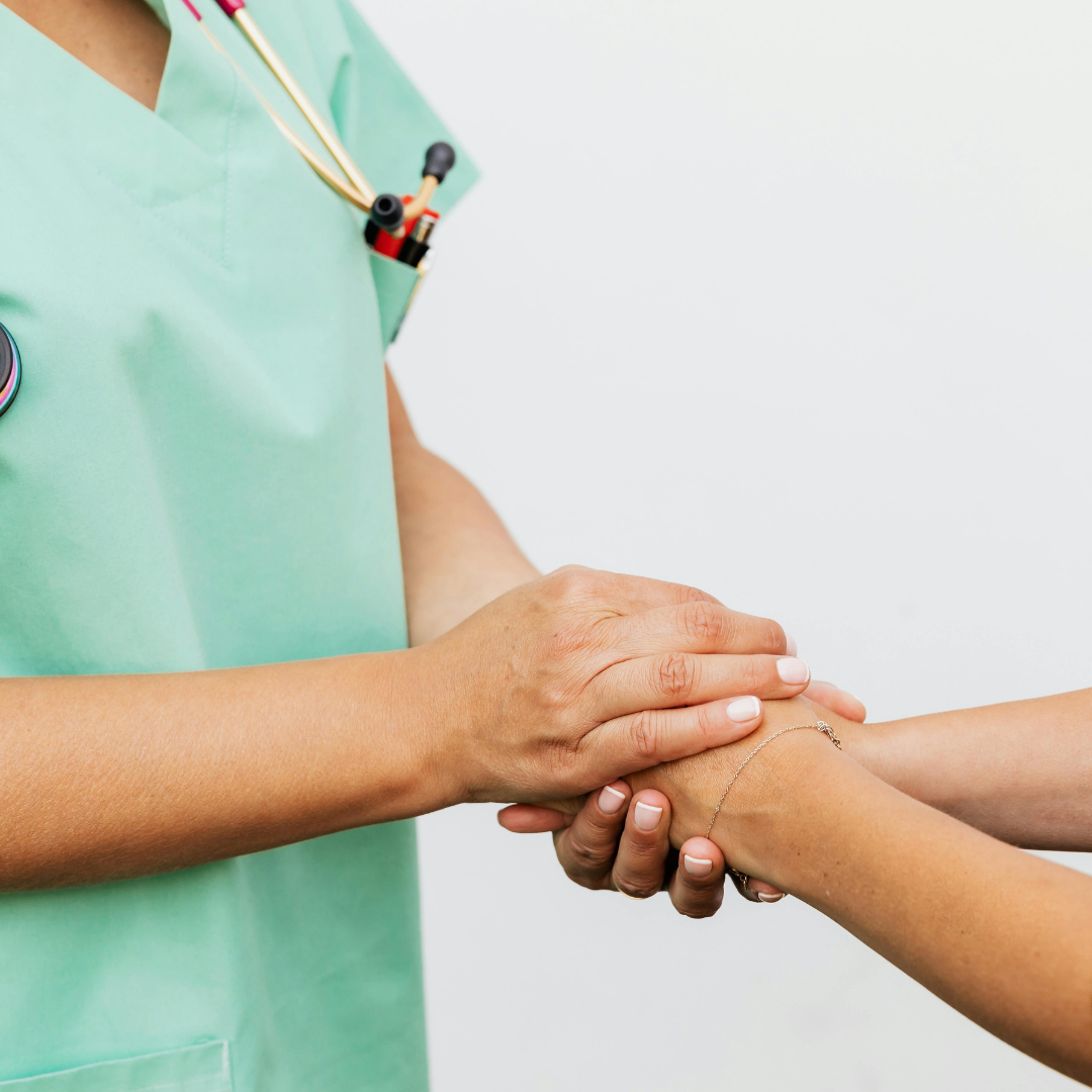 A healthcare professional in a green uniform holding and examining a patient's wrist, with a stethoscope visible around their neck.