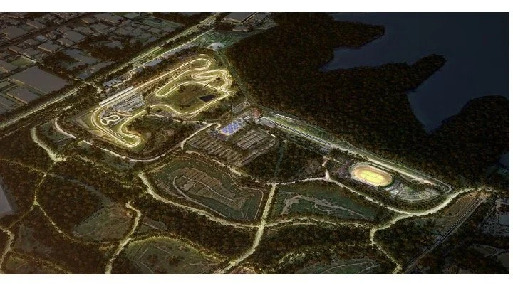 Aerial view of an illuminated racetrack complex at night surrounded by trees and dark water.