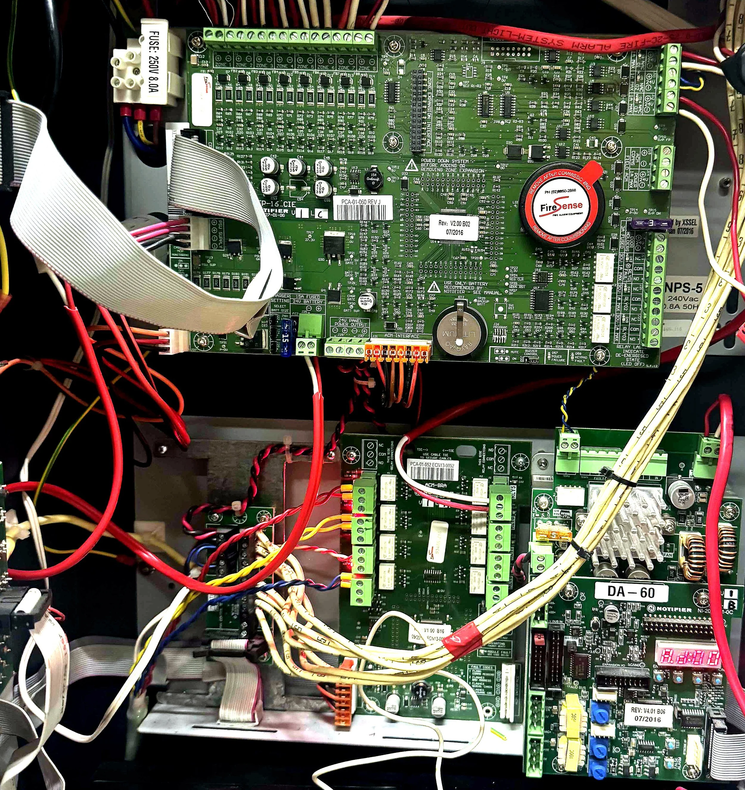 Electrical control panel with green circuit boards, various colored wiring, capacitors, connectors, and labels.