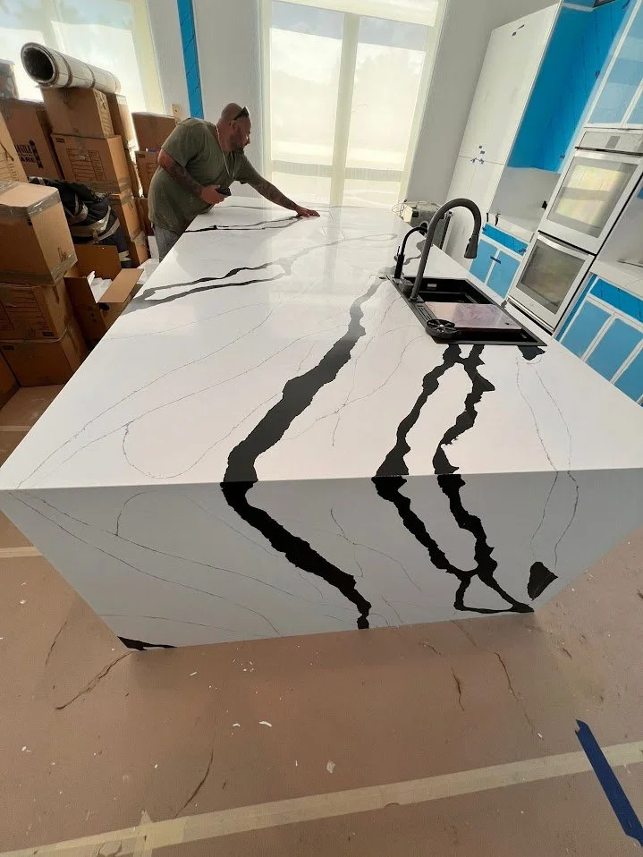 A man working on a kitchen island with a white marble pattern featuring black veining.