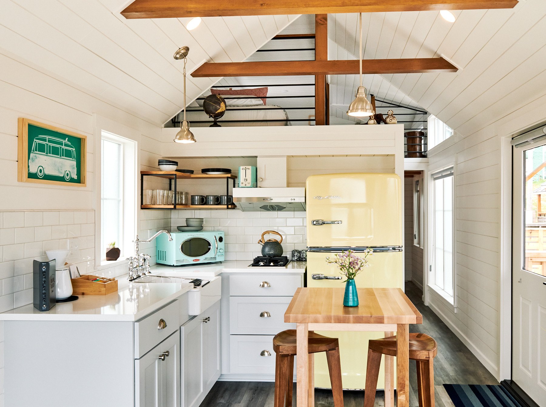 Modern tiny house kitchen at Dillon Beach Resort with retro appliances, loft bed, and butcher block dining table.