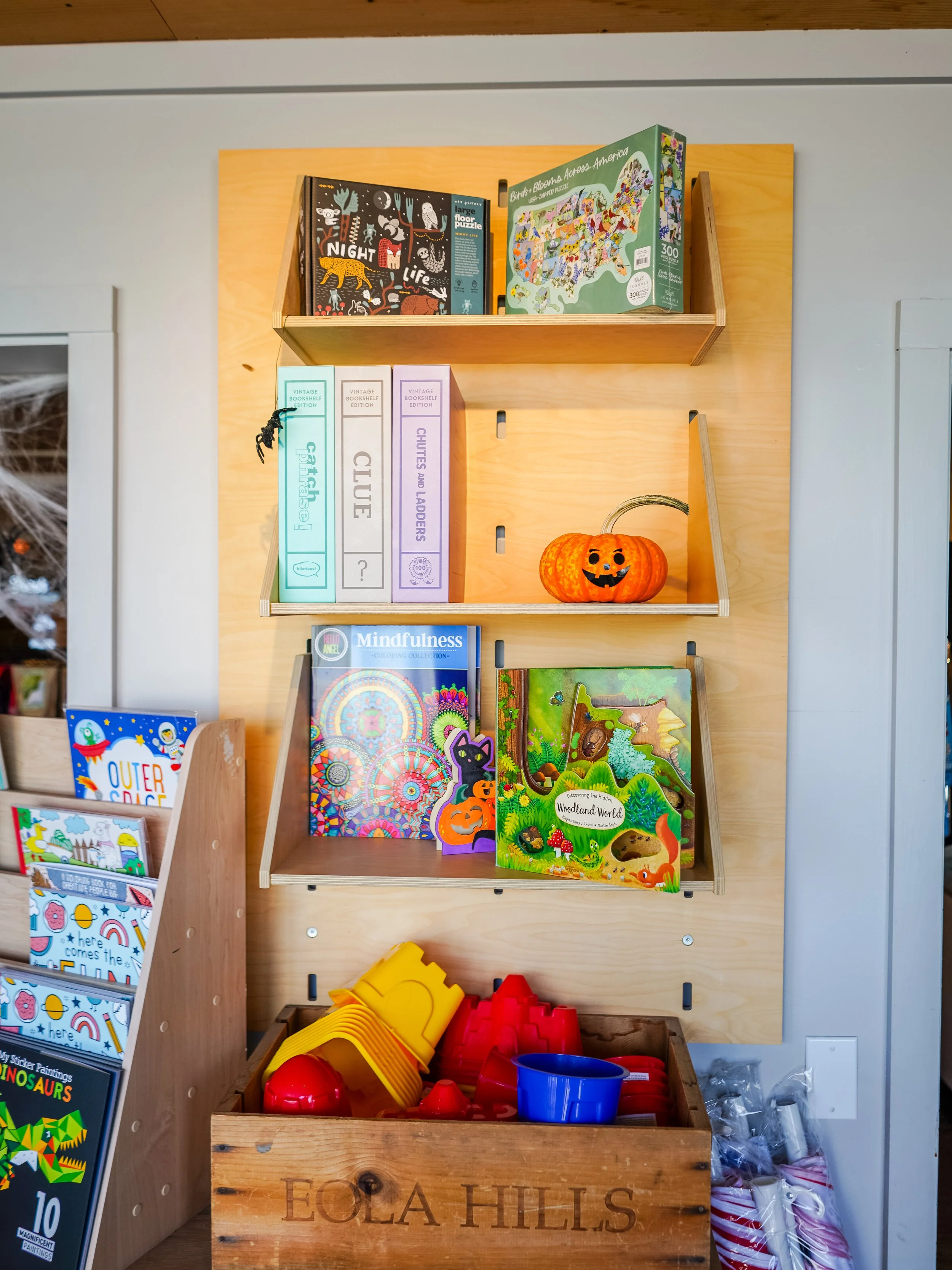 Wooden shelf with children's books, a pumpkin-shaped container, and plastic toys in a store display.