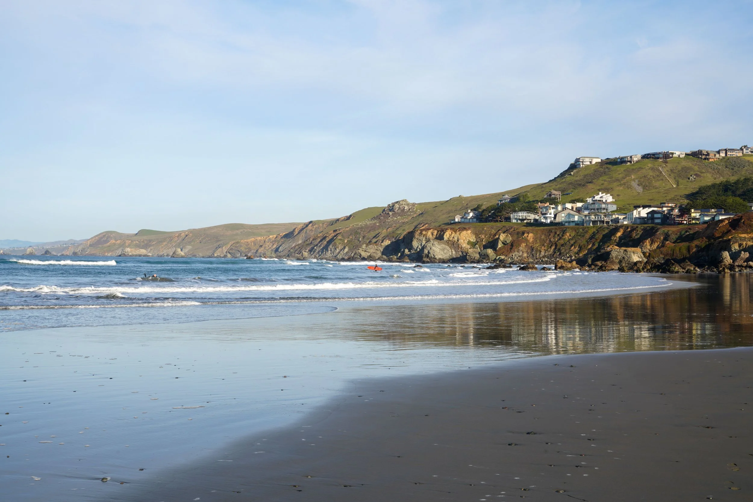 Beach with waves and a hillside with houses overlooking the ocean.