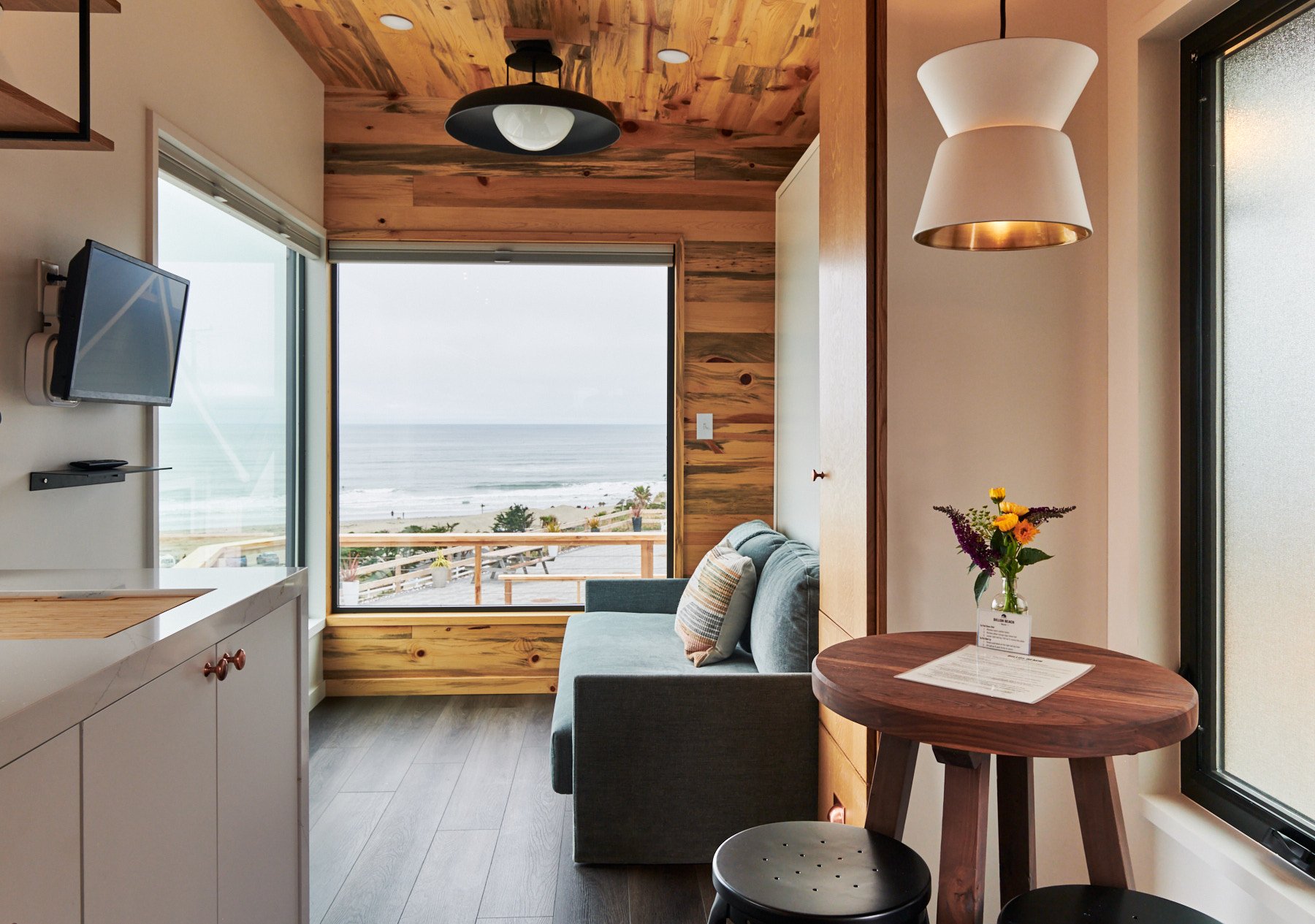 Modern coastal cabin interior at Dillon Beach Resort with an ocean view window, teal sofa, and wood paneling.
