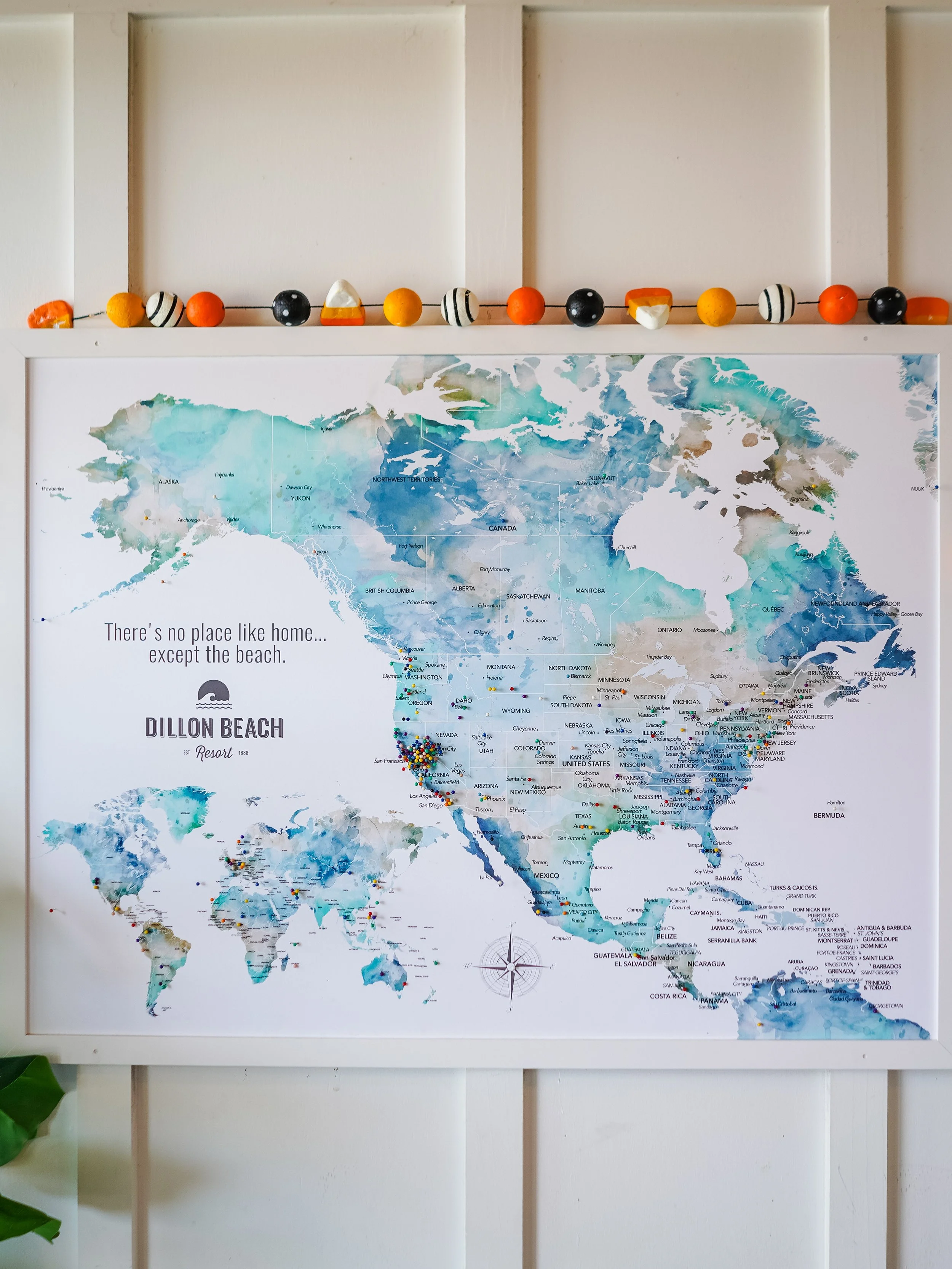 A map of North America, Central America, and parts of South America, with the text "There's no place like home... except the beach." and the Dillon Beach Resort logo. There is a string of decorative beads or balls on the shelf above the map.