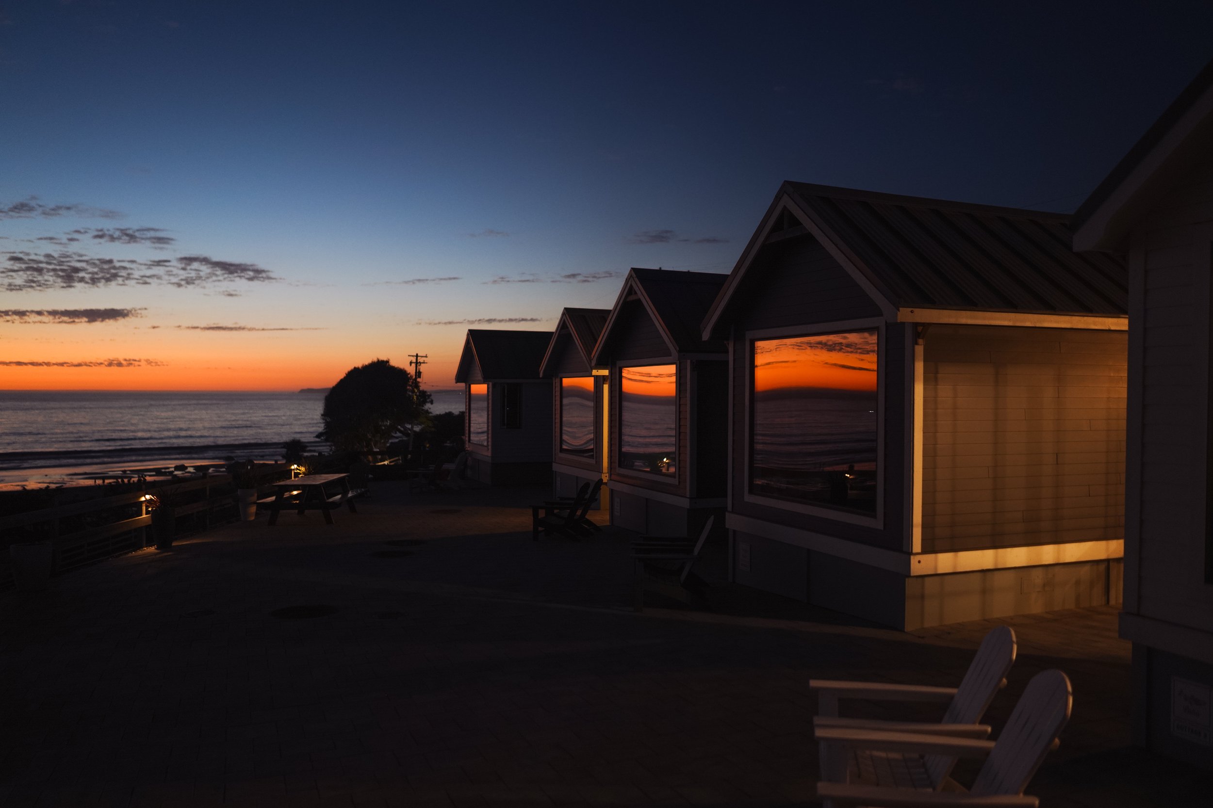 Beachside cottages at sunset with reflections on windows and calm ocean in the background.