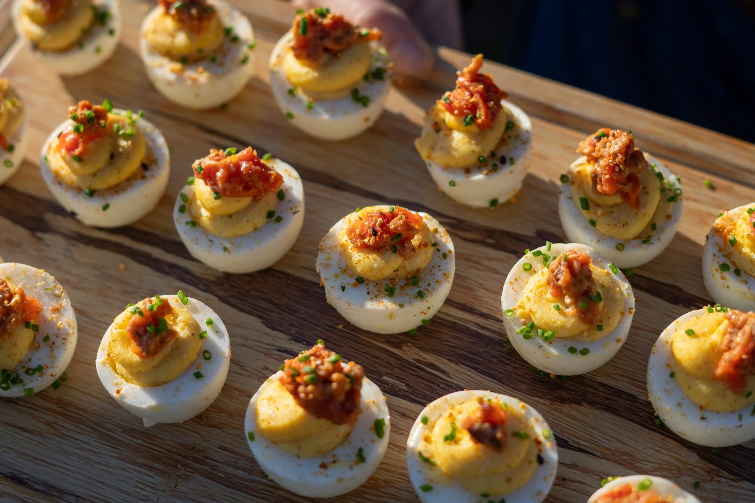Gourmet deviled eggs topped with sun-dried tomato and fresh chives, served on a wooden platter for a catered event at Dillon Beach Resort.