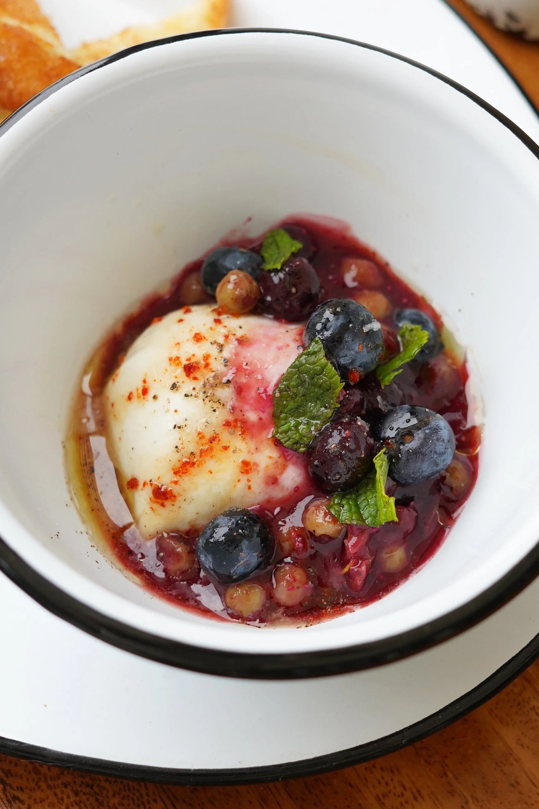 A bowl of mixed berries topped with a poached egg, garnished with mint leaves and sprinkled with paprika.